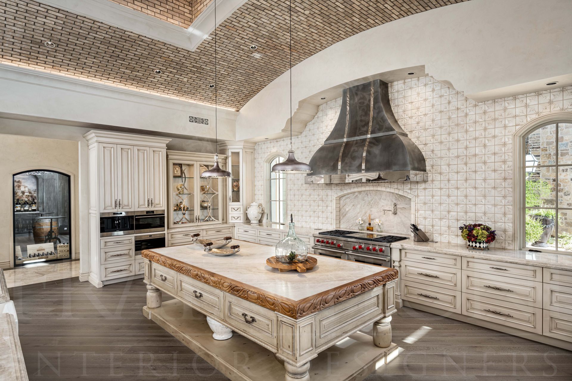 Bright, luxury kitchen with a large custom island, ornate range hood, white cabinets, and a mosaic tile backsplash