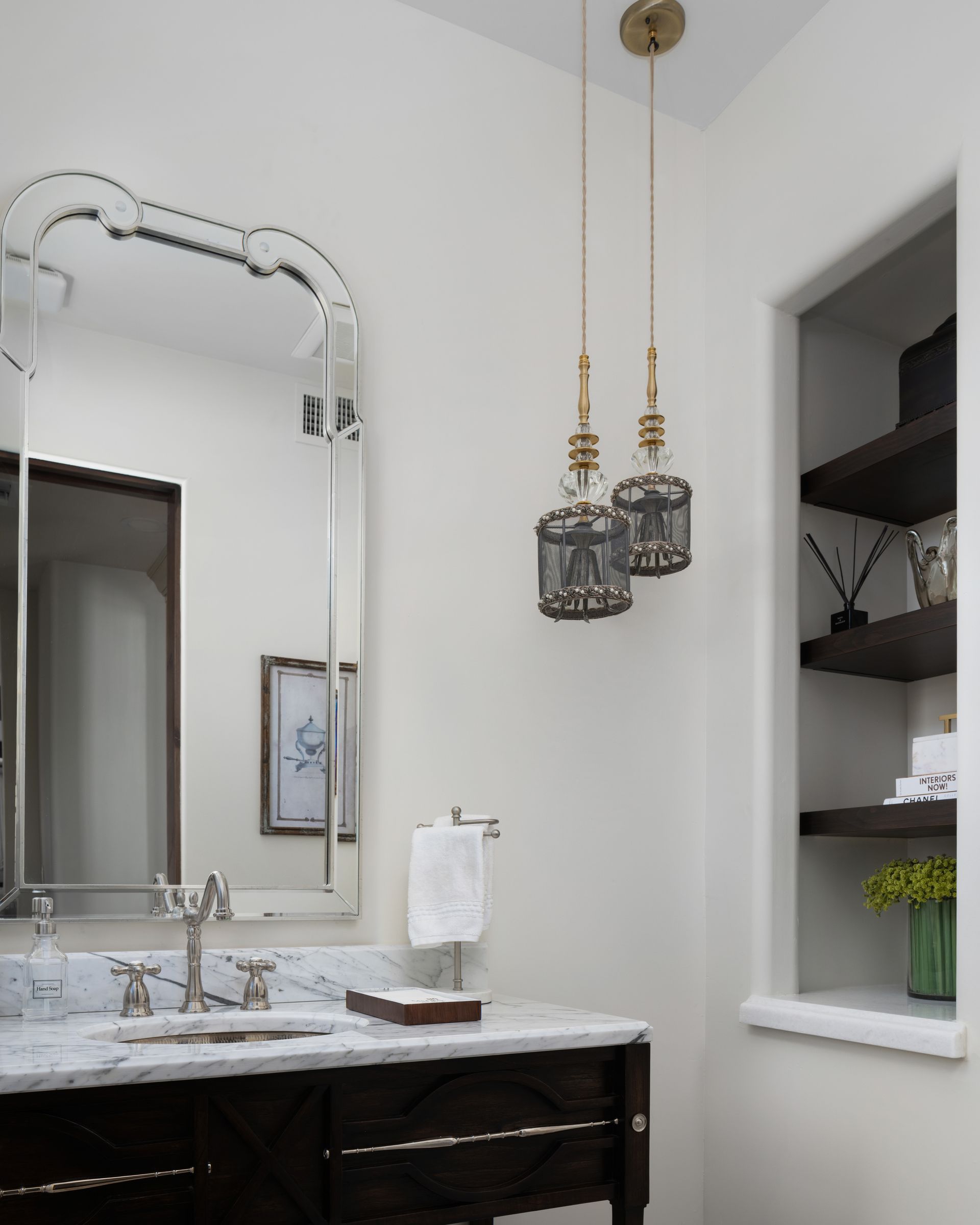 Bathroom with ornate mirror, pendant lights, dark vanity, and built-in shelving.