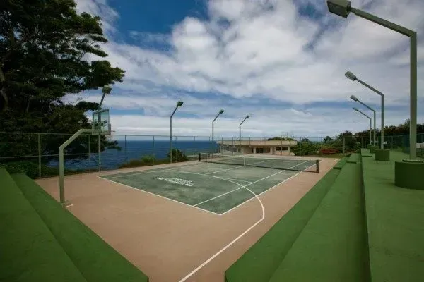 Basketball and tennis court on a hill overlooking the ocean, lit by streetlights under a cloudy sky.