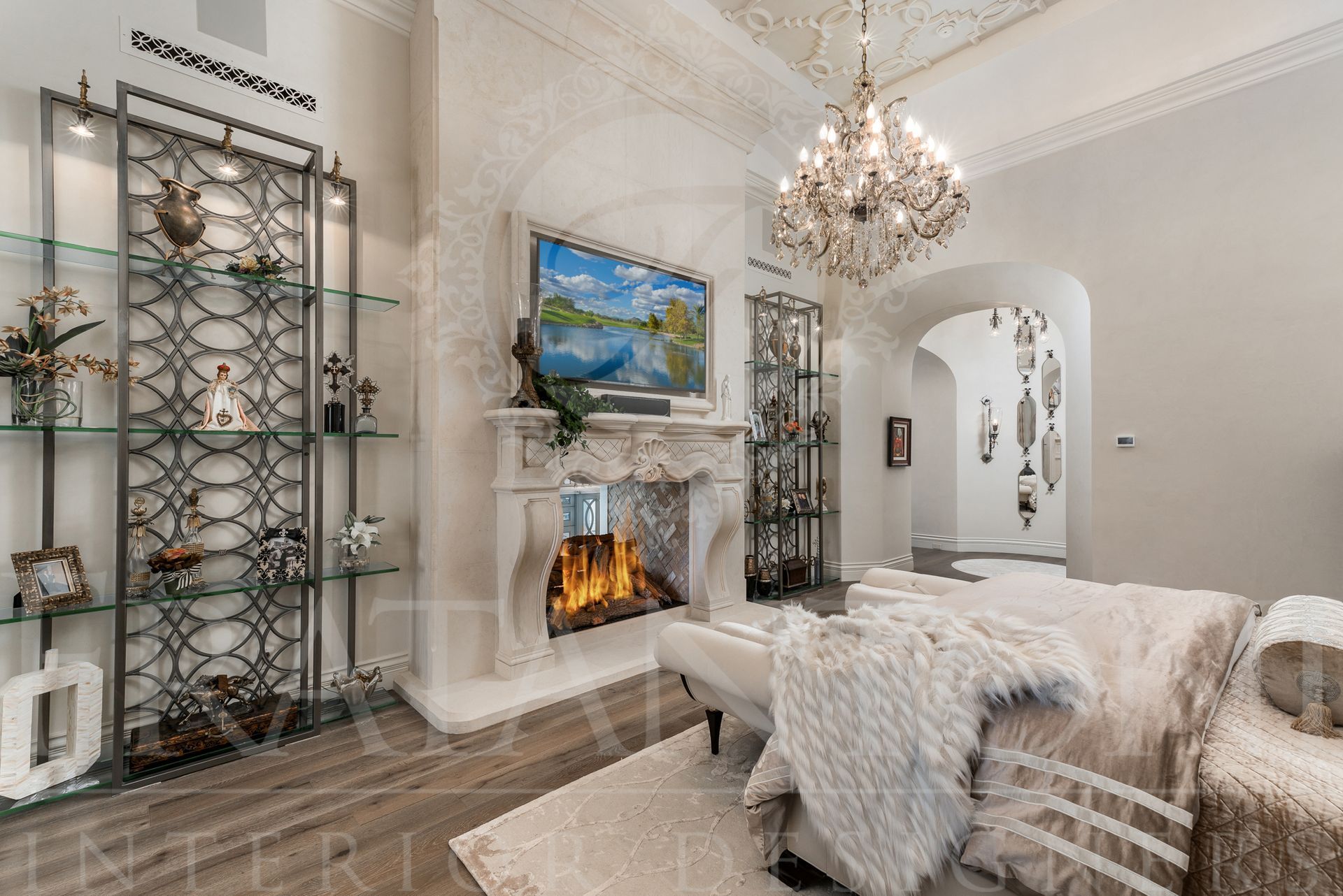 Luxurious primary suite with stone fireplace, chandelier, shelving, wood floors, and white furniture.