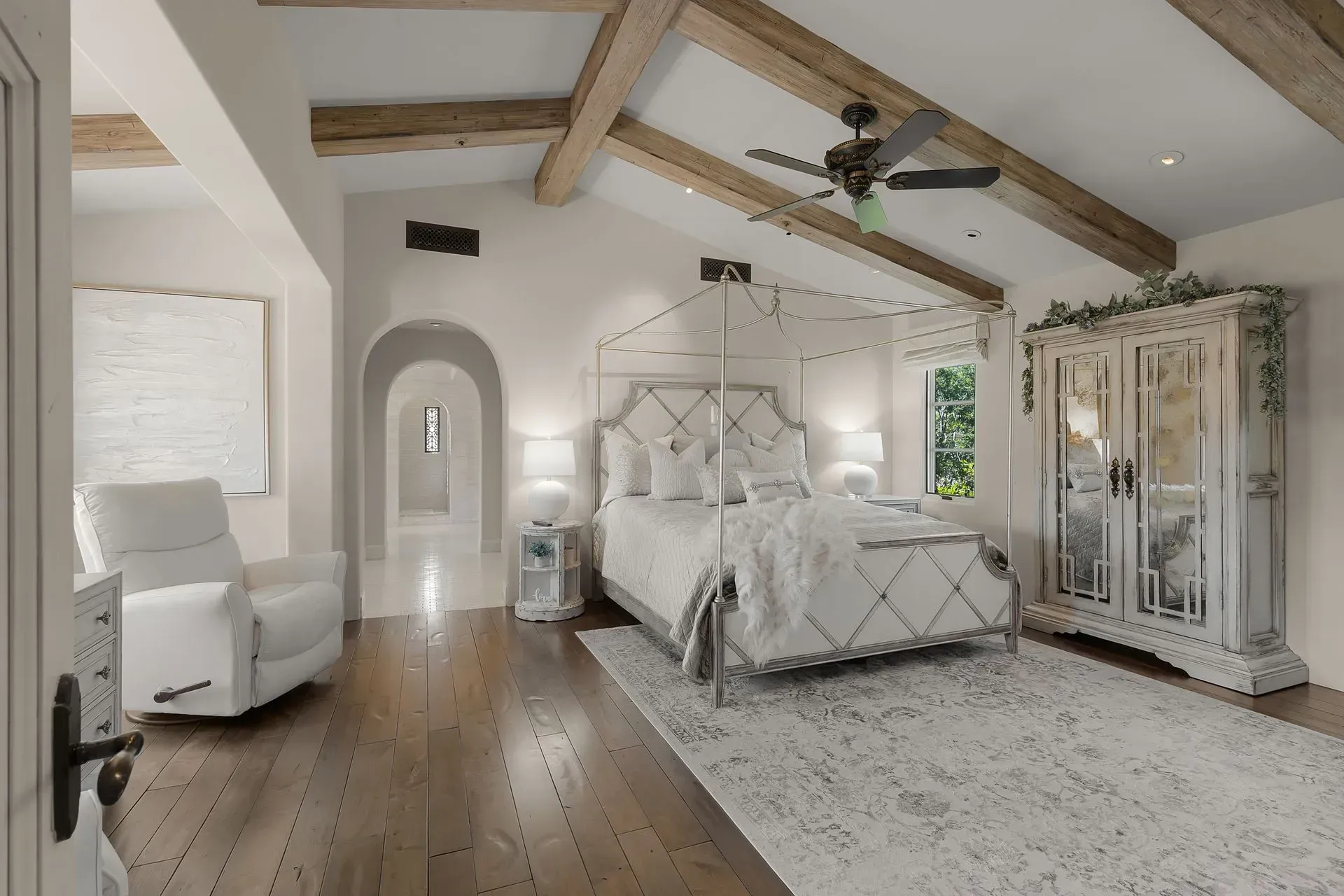 Spacious bedroom with white bed, wooden beams, and white recliner.