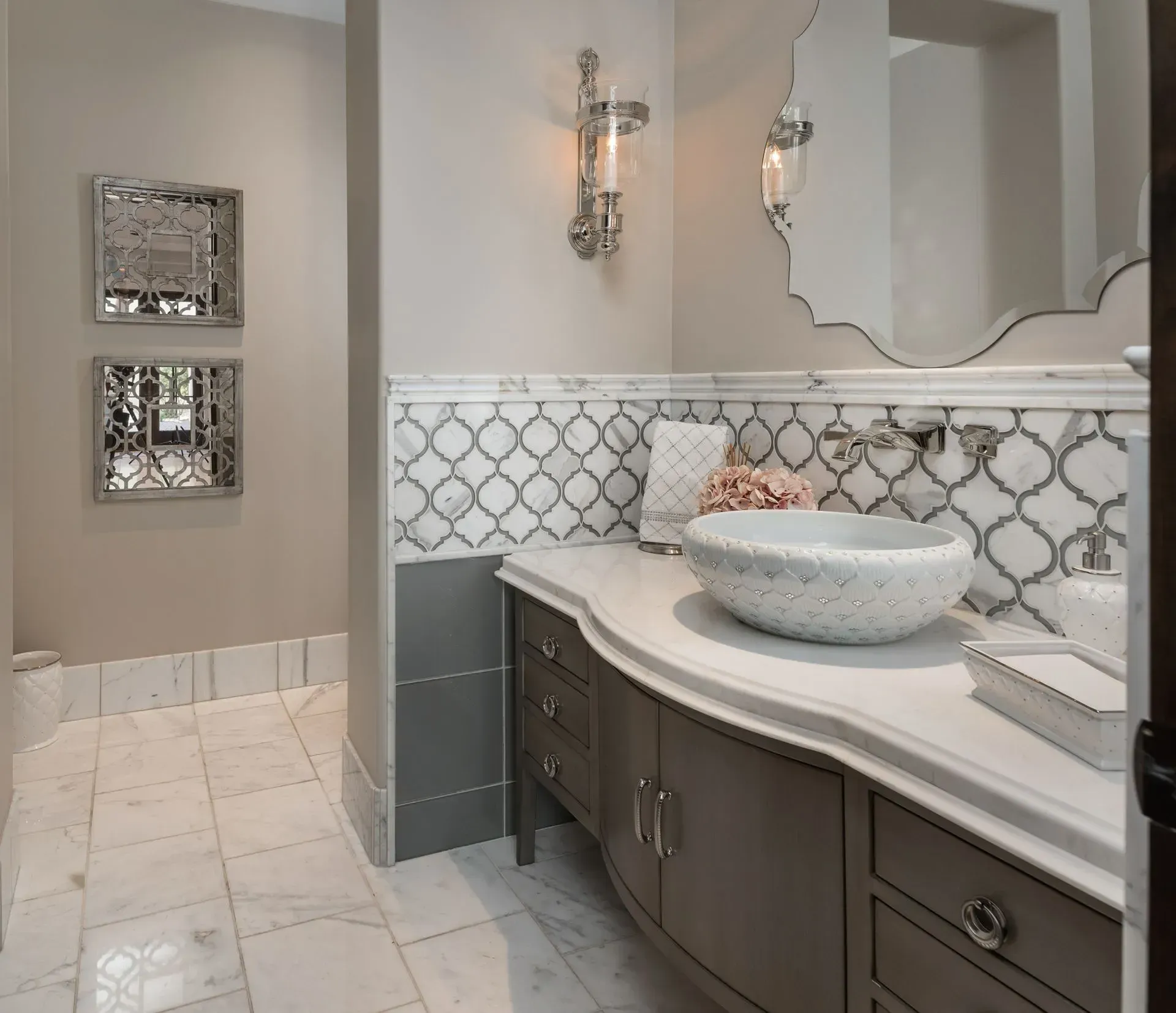 Elegant bathroom with curved vanity, patterned backsplash, decorative mirrors, and bowl sink.