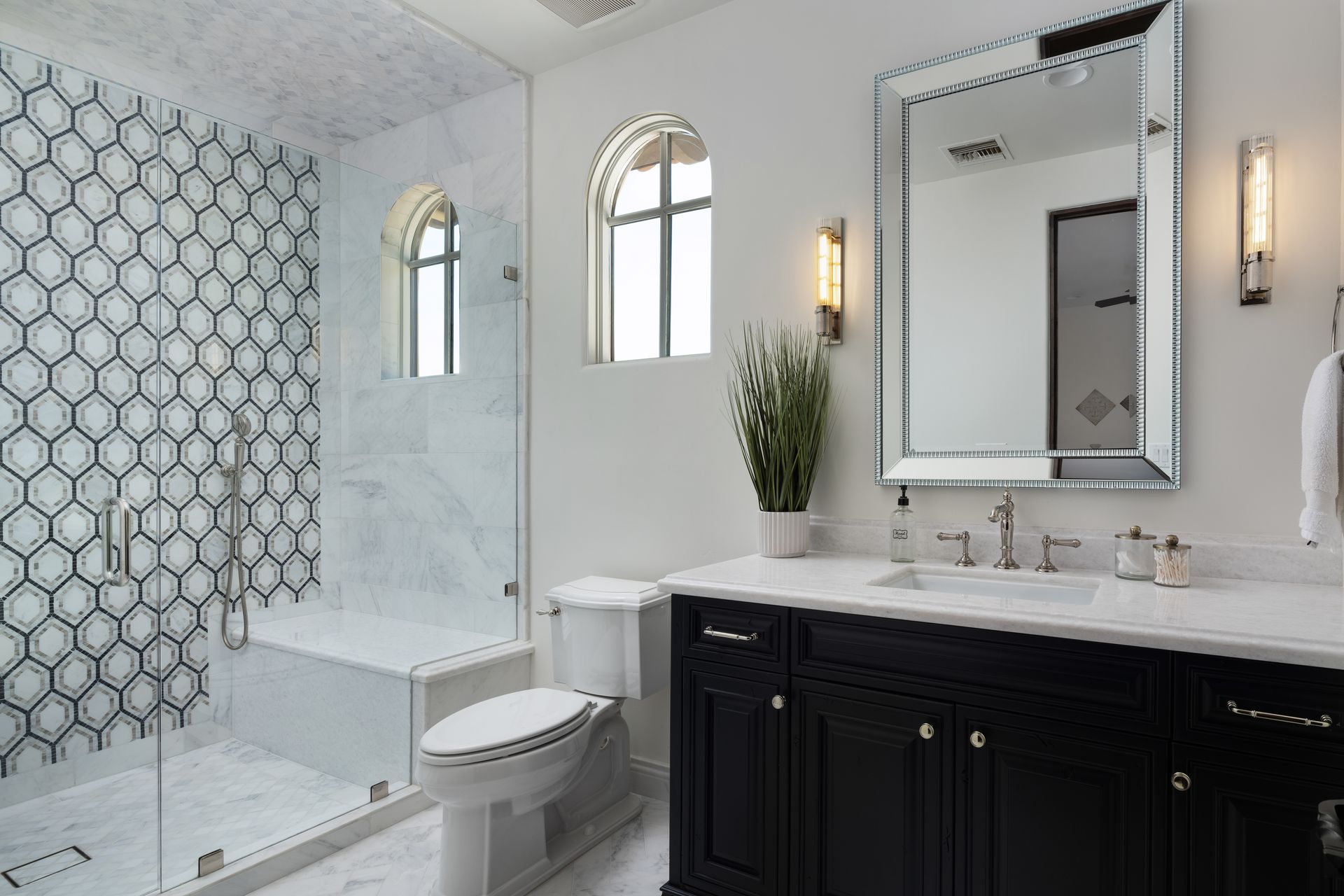 Luxurious bathroom with black vanity, patterned shower tile, and large mirror.