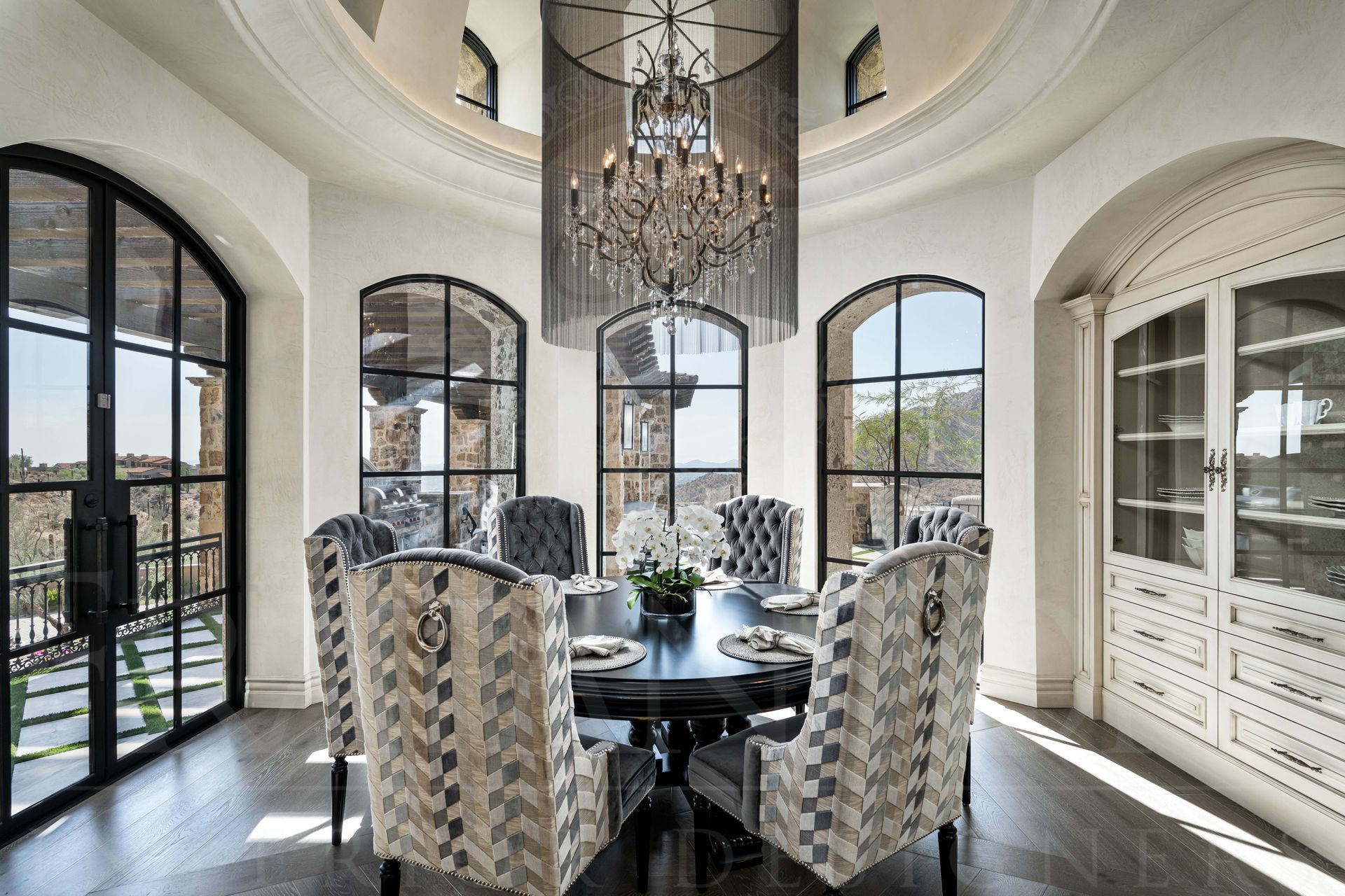 Elegant breakfast nook with arched windows, panoramic views, statement chandelier, and a round table with patterned chairs