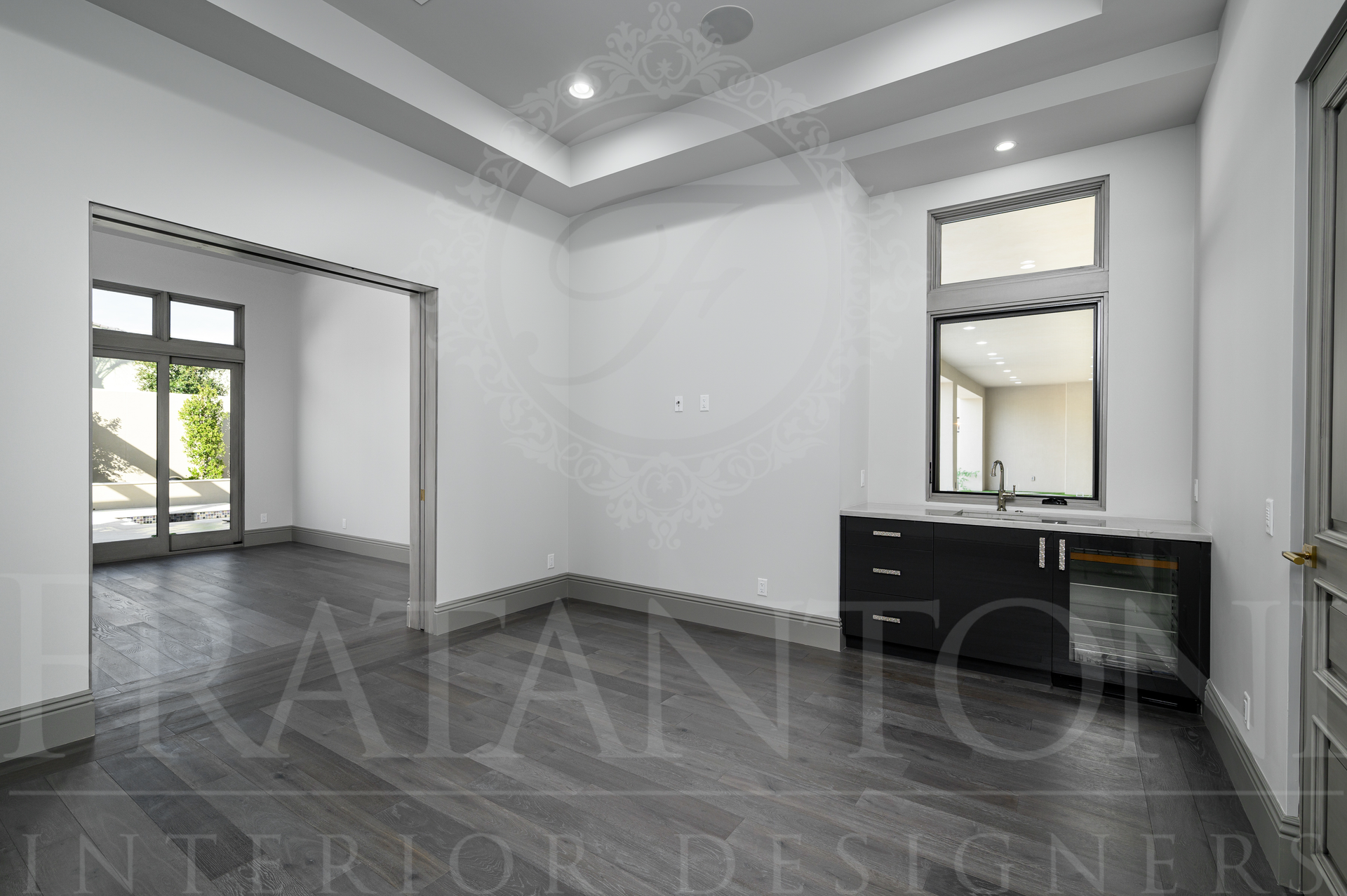 Luxury living room with dark wood floor, white walls, and a wet bar overlooking the backyard.