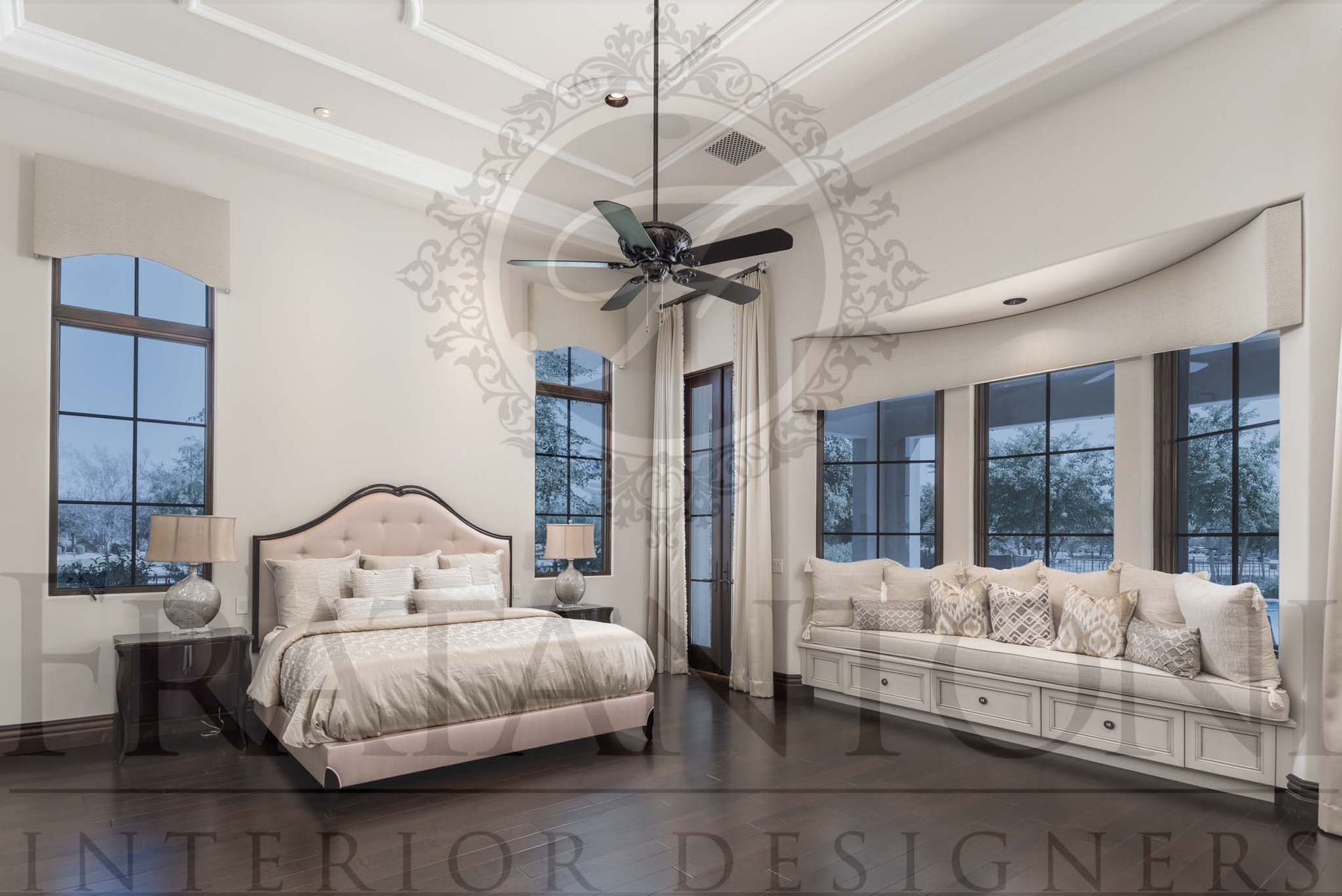 Elegant bedroom with a large bed, curved window seat, ornate ceiling, and black ceiling fan in a bright, white interior with dark wood floors.