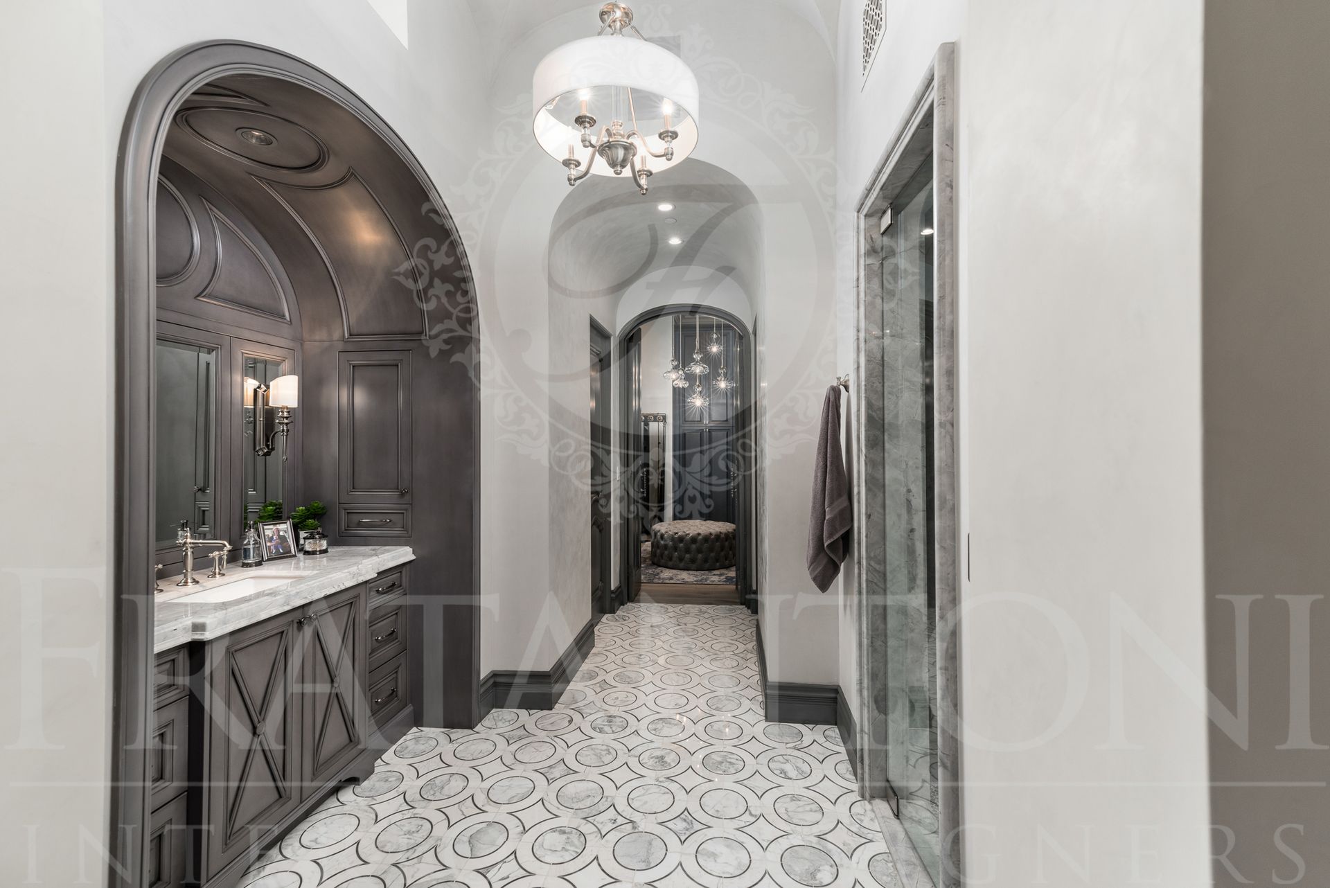 Primary suite bathroom with gray and white decorative floor tiles, an inset arched vanity, walk in shower, leading to a closet with decorative gray accents.
