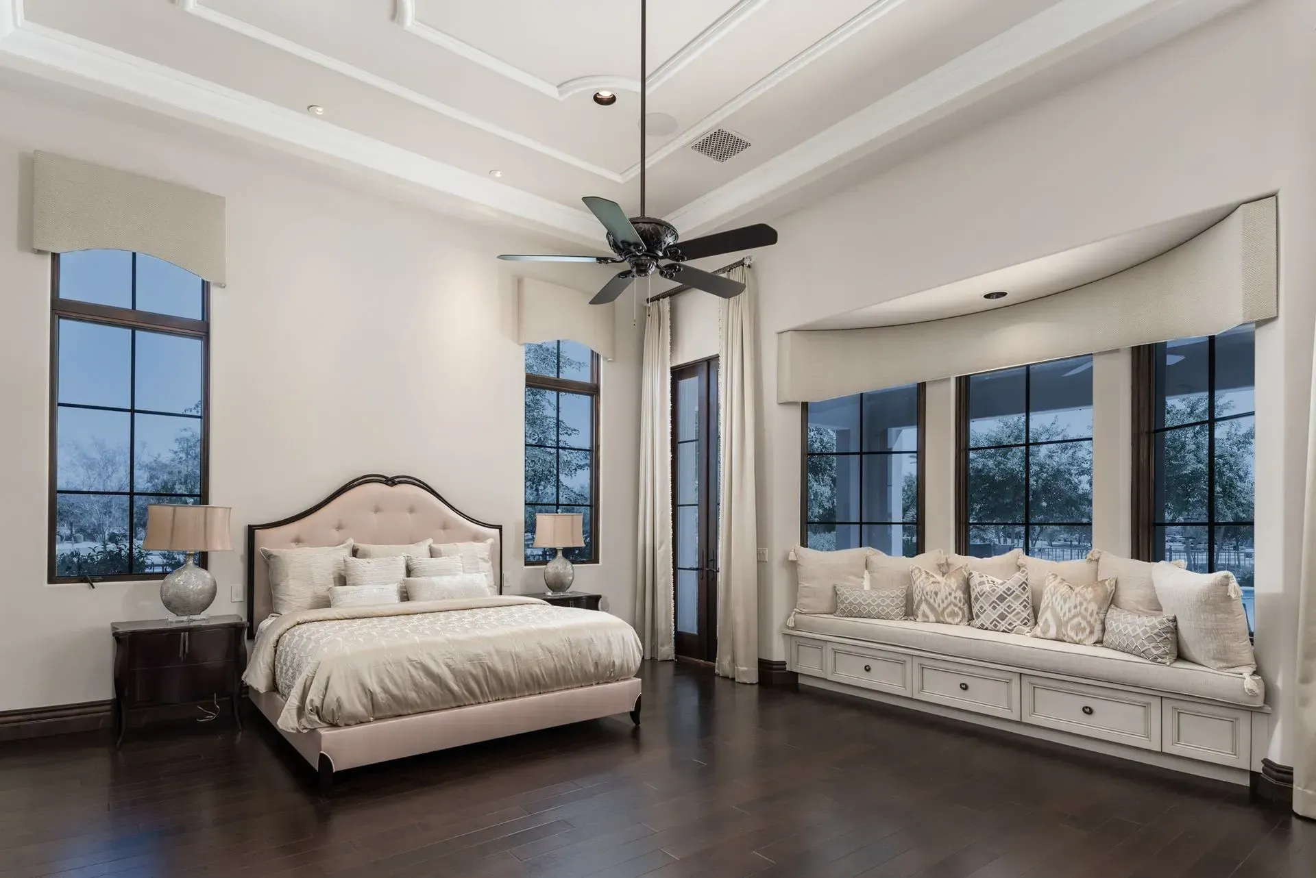 Spacious bedroom with a bed, bench seating, large windows, and dark hardwood floors.