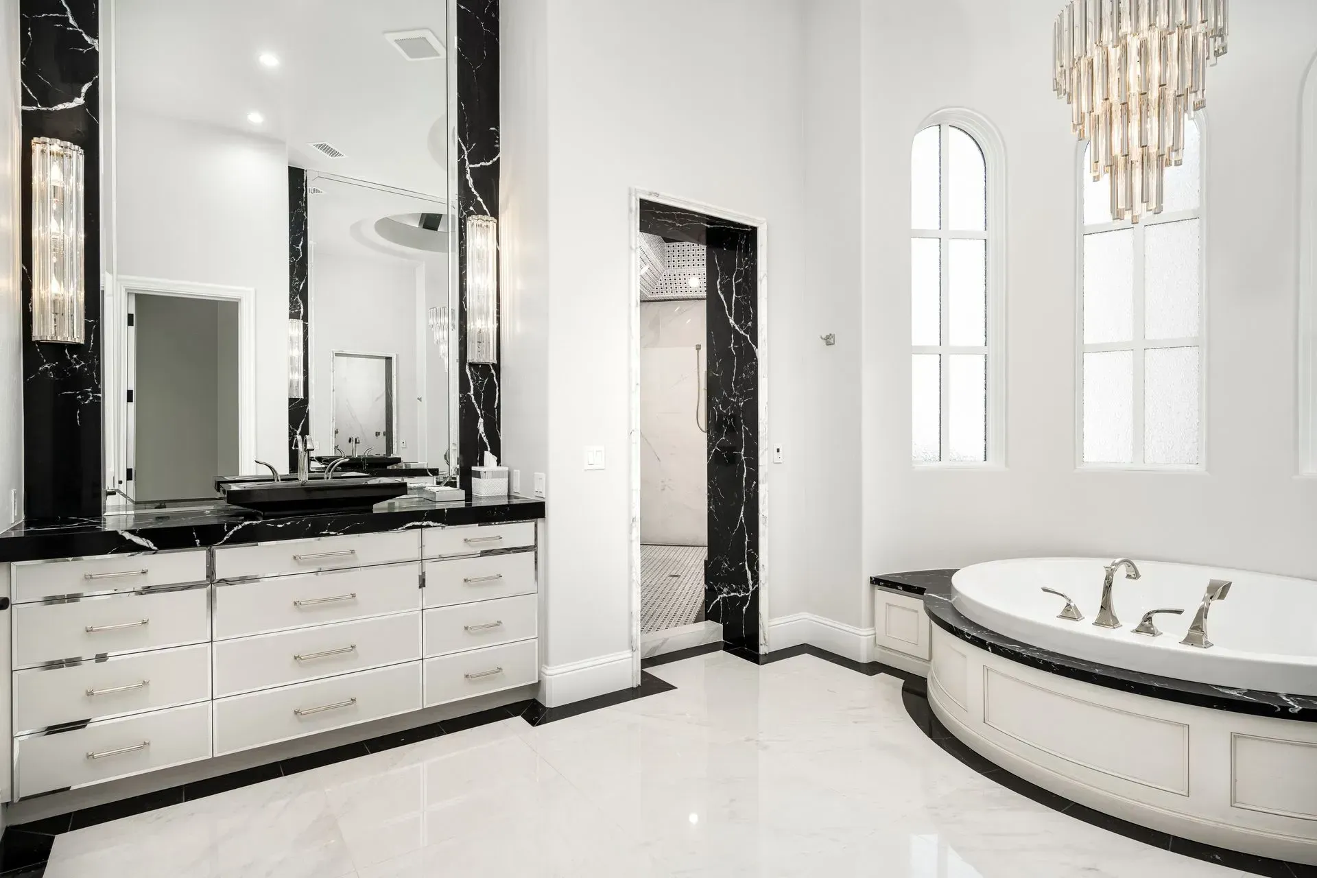 Luxurious white and black bathroom with a bathtub, dual sinks, and a large mirror.