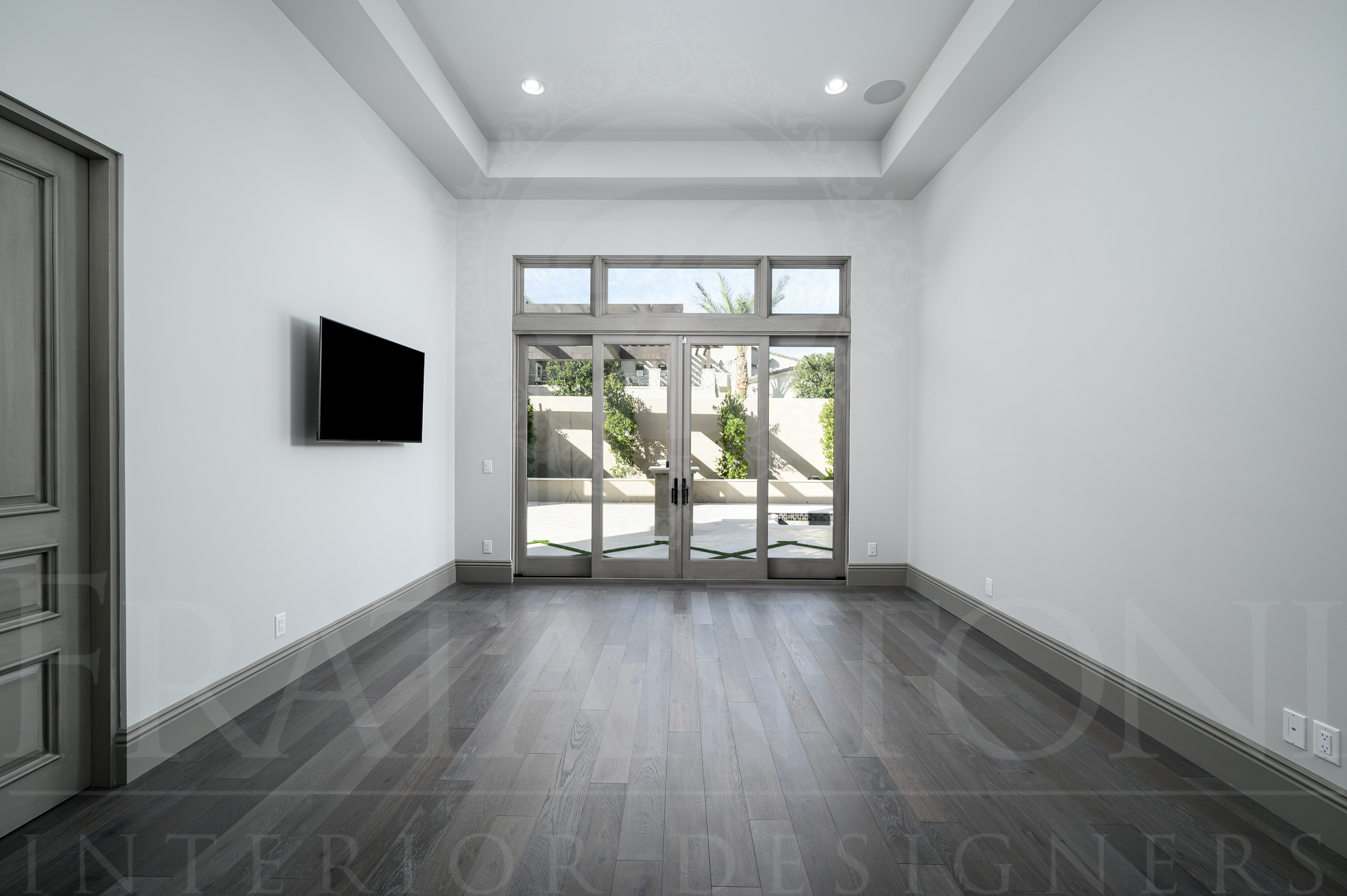 Elegant living room with dark wood floor, white walls, wall-mounted TV, and glass doors to a courtyard in Scottsdale, Arizona