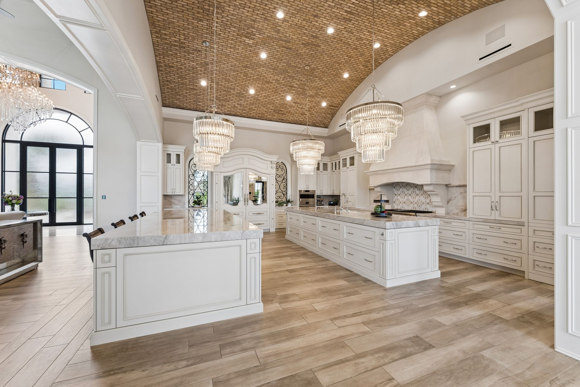 Luxury kitchen with brick ceiling, dual marble islands, and custom hidden fridge under chandeliers