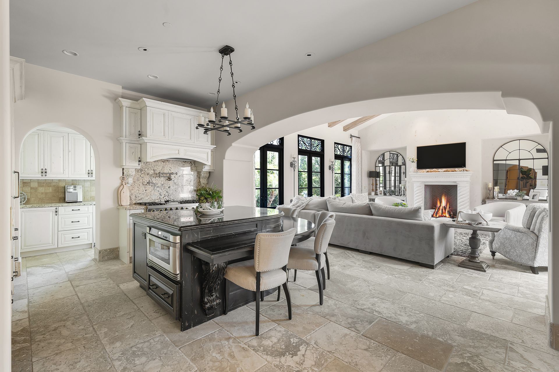 Elegant open-concept living and dining room with fireplace, arched windows, and neutral furnishings