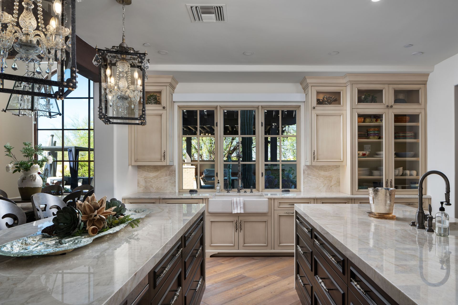 Upscale kitchen with two islands, light countertops, dark cabinets, and crystal chandeliers.
