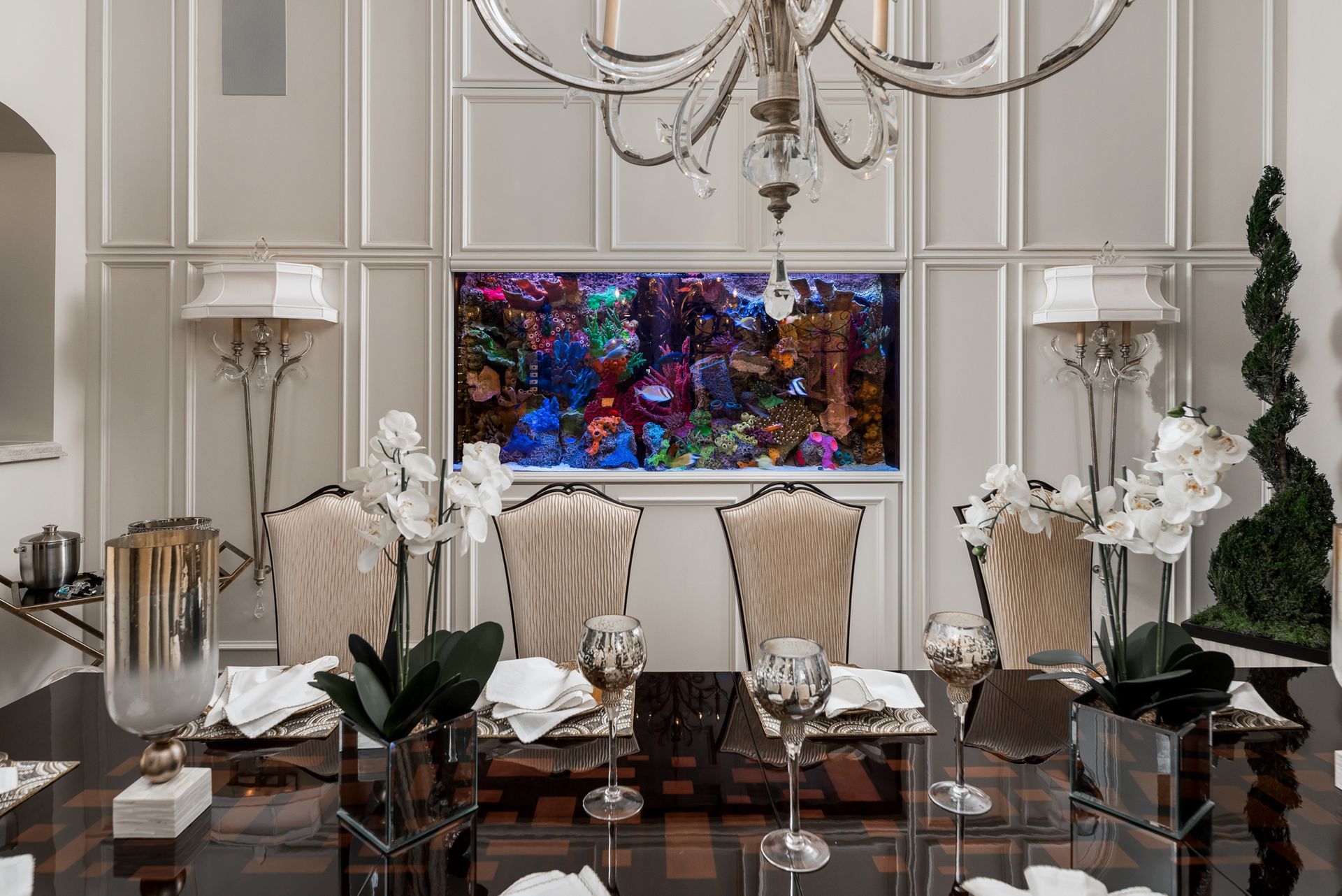 Elegant dining room with large aquarium built into paneled wall. Formal table setting, crystal chandelier.