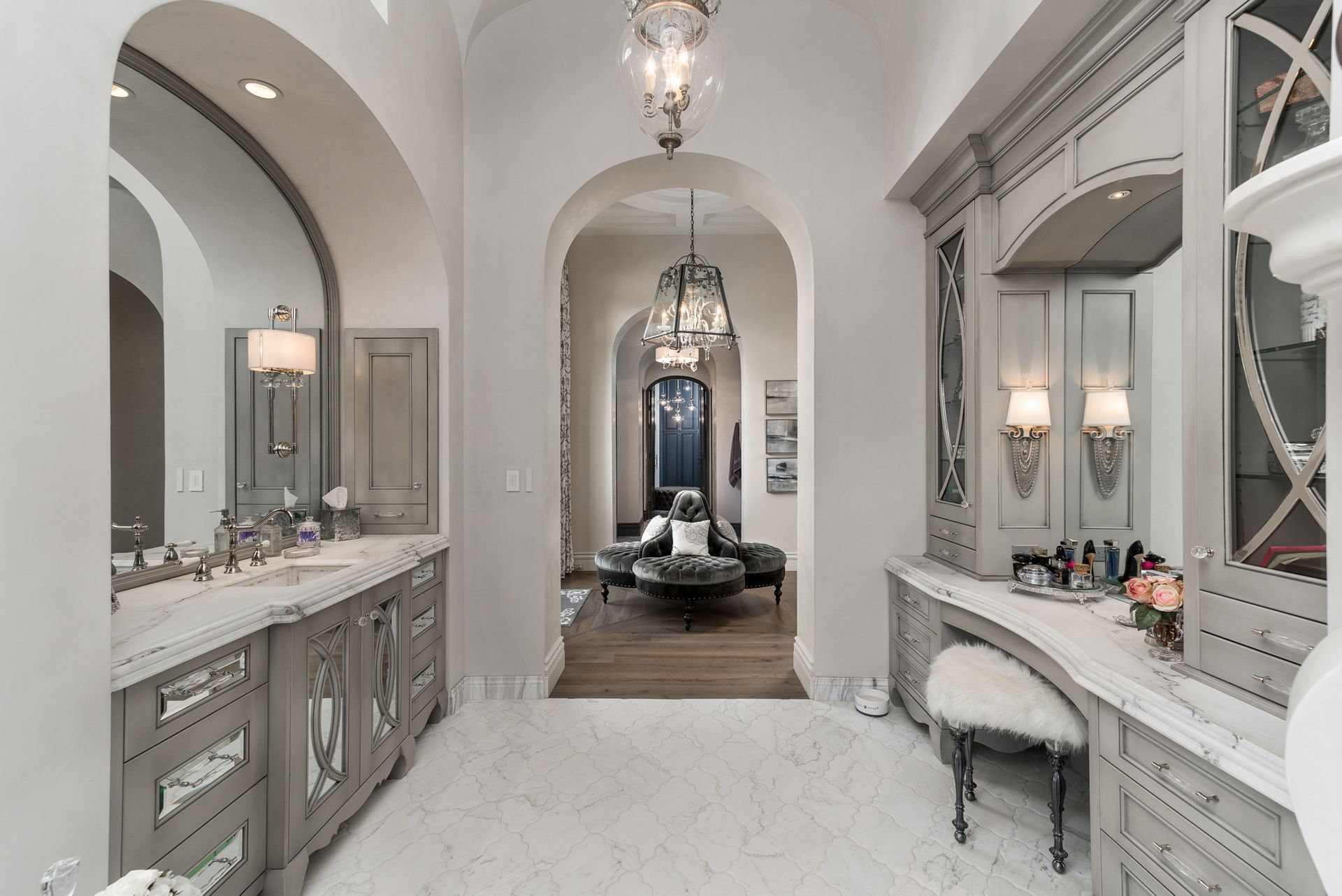Elegant, gray-toned bathroom with vanity, arched doorways, and chandelier.