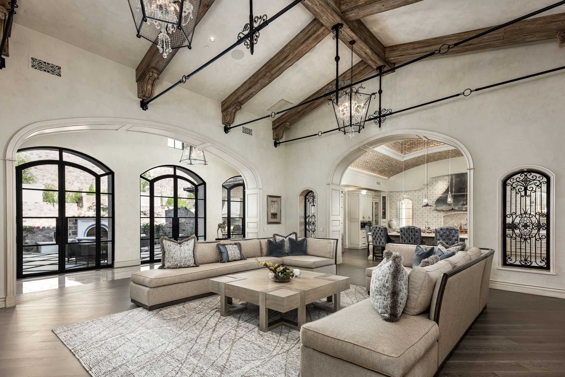 Spacious living room with vaulted ceiling, arched windows, light-colored couches, and wooden beams.