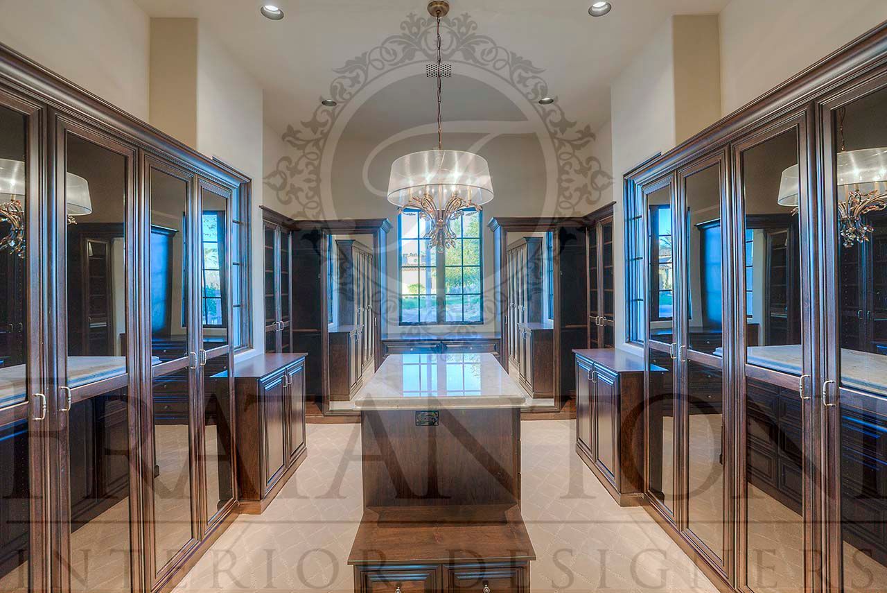 Luxury custom walk-in closet interior with glossy dark wood glass cabinets, marble island, and chandelier-lit with large window.