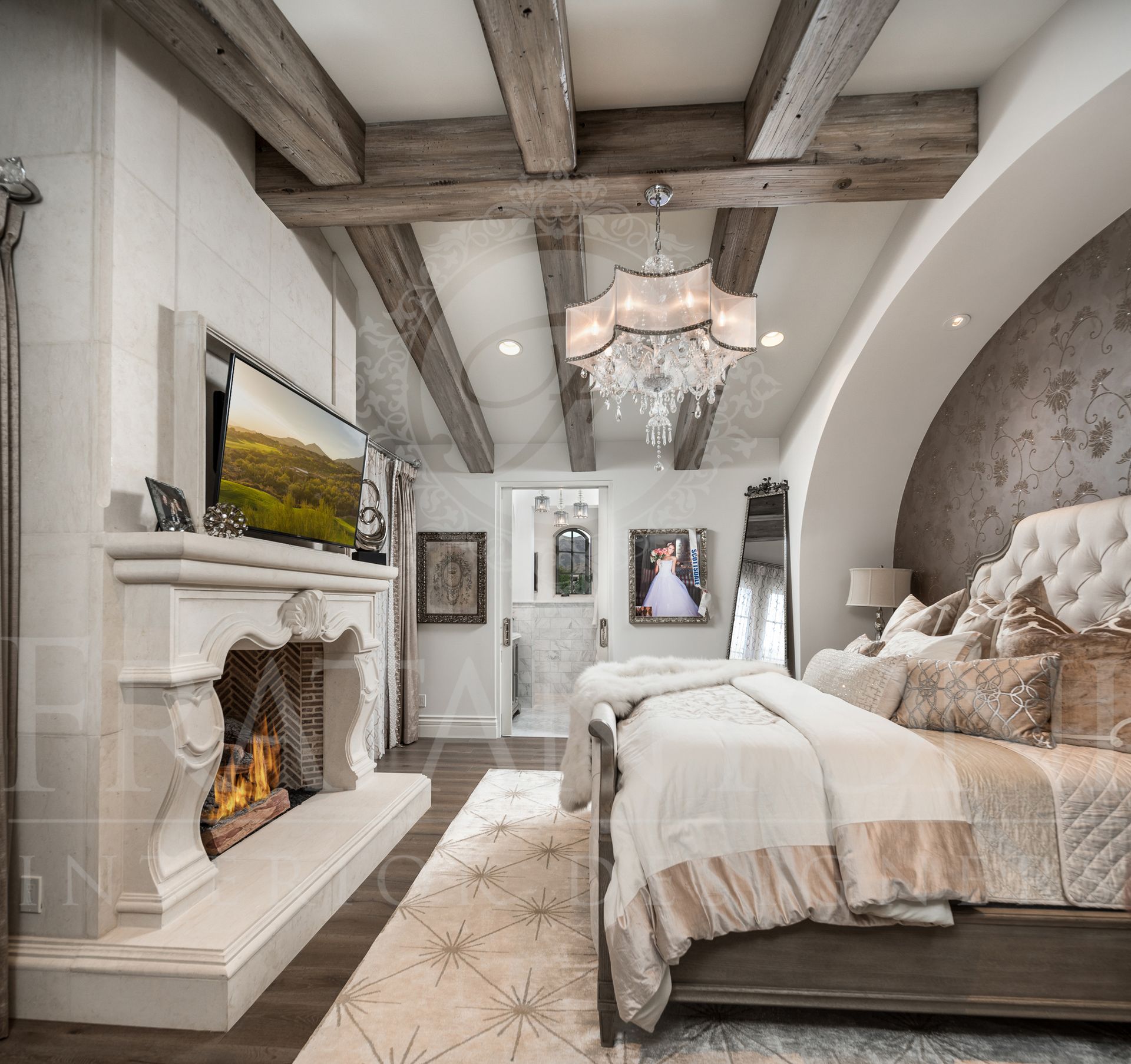 Luxurious bedroom with fireplace, chandelier, wood beams, and large bed with decorative pillows and blanket designed by Fratantoni interior designers in scottsdale Arizona