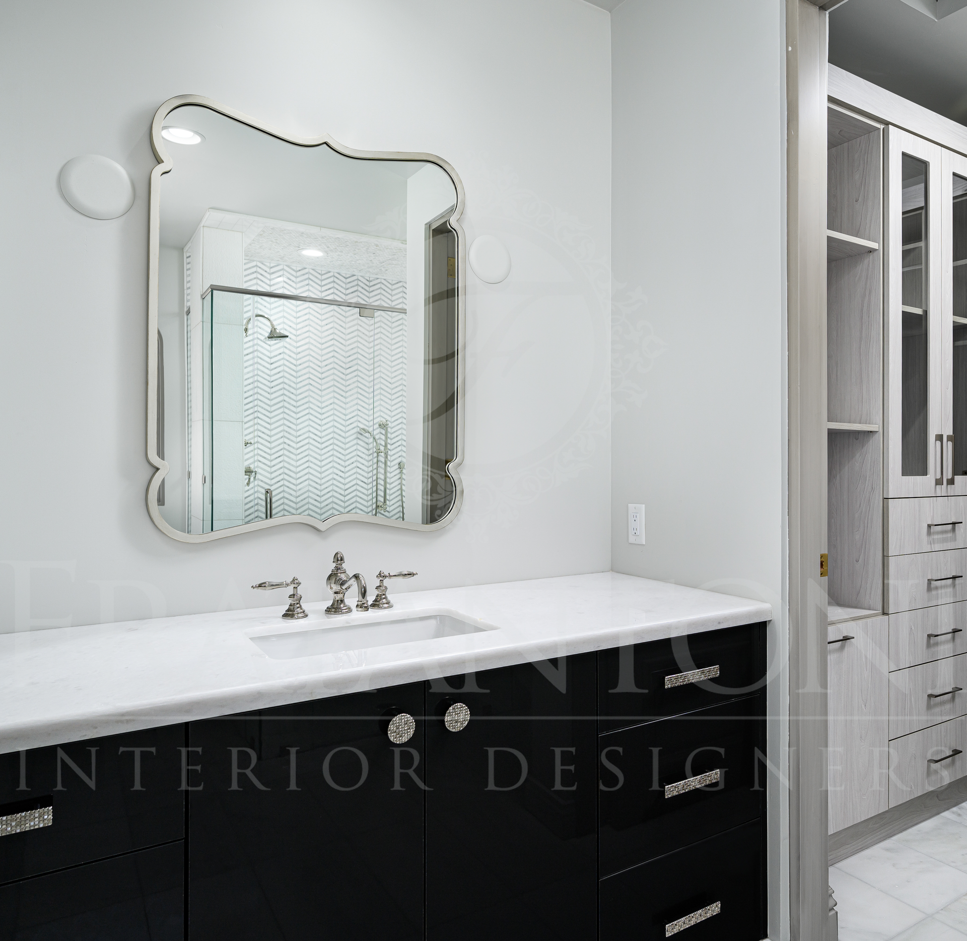 Modern bathroom with white counters, a black custom vanity, ornate framed mirror, and dark cabinetry beside a custom walk-in closet.