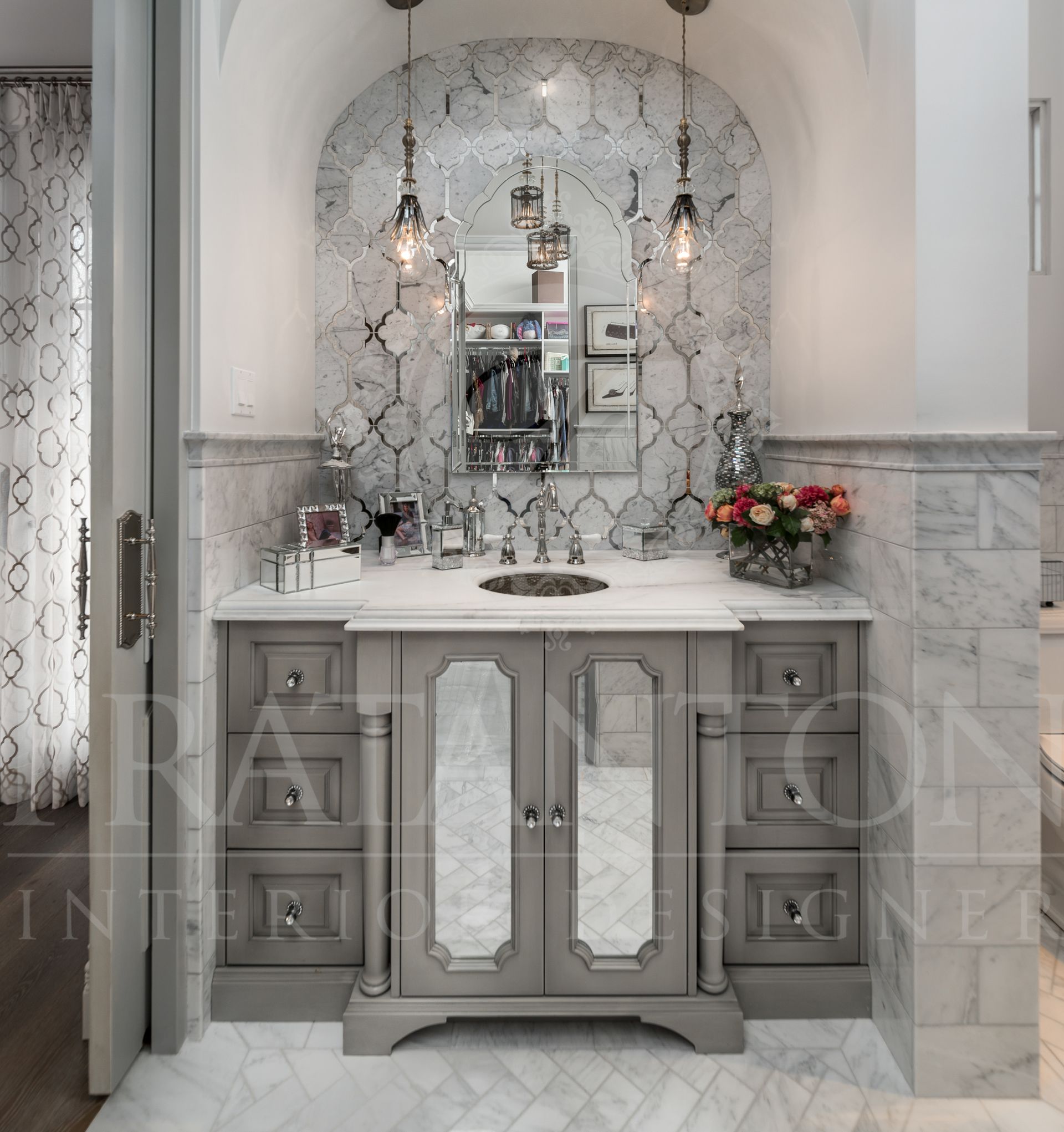 Gray vanity with marble countertop and mirror, beneath two pendant lights, in bathroom.
