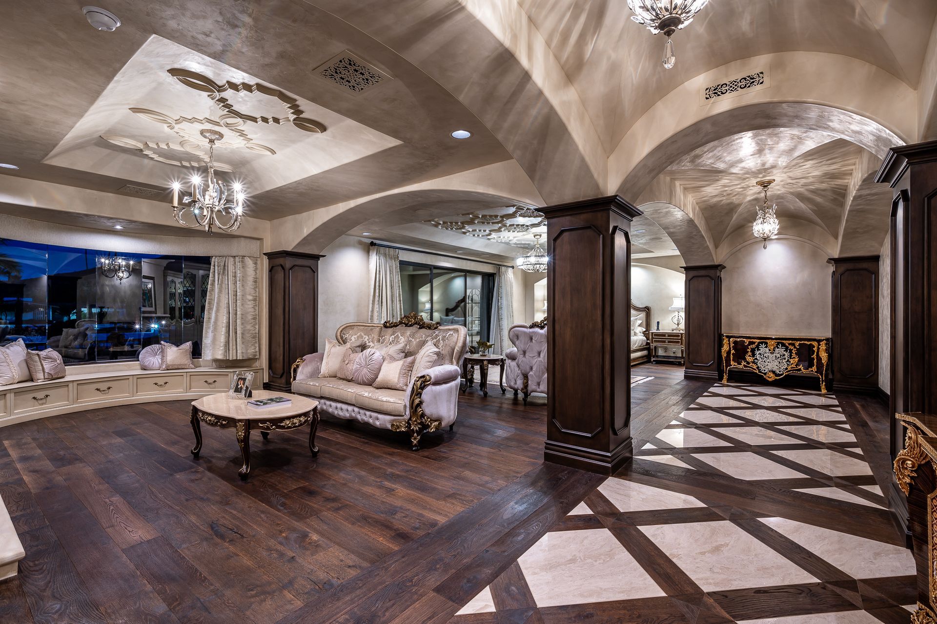 Luxury Interior design master suite
with arched ceiling, chandeliers, sofas, and dark wood floors
