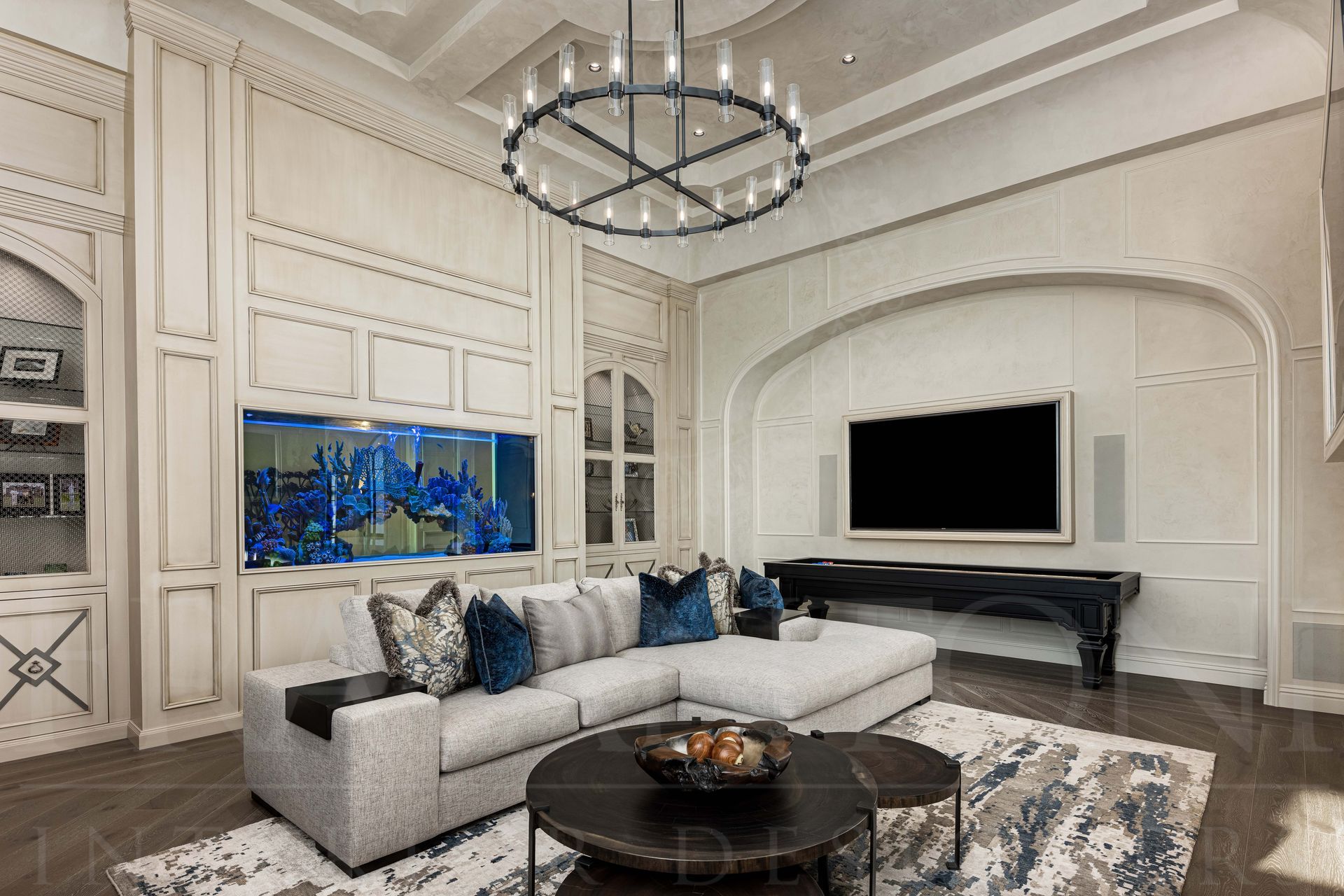 Elegant white living room with a sectional sofa, black coffee table, chandelier, and wall-mounted TV with a custom in-wall luxury fish tank