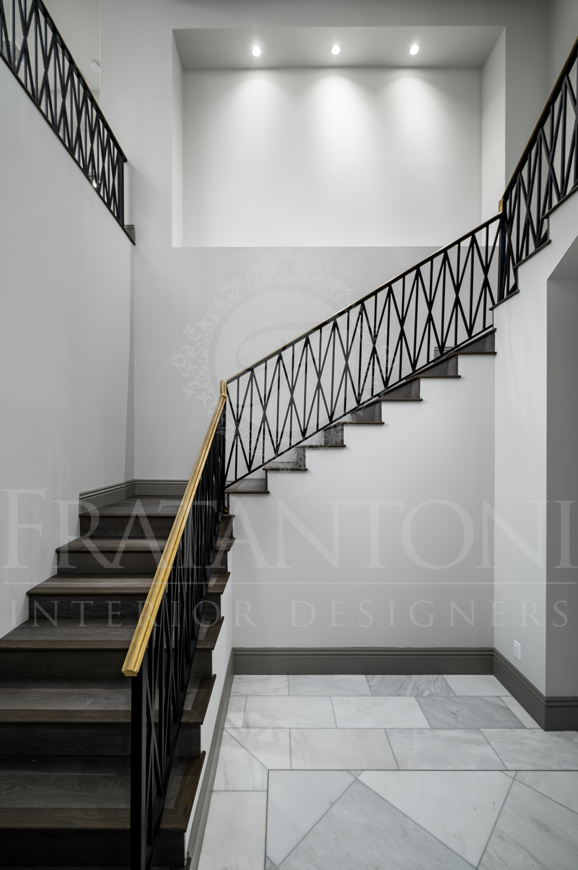 Elegant indoor staircase with black steps, gold handrail, and white walls in a modern foyer