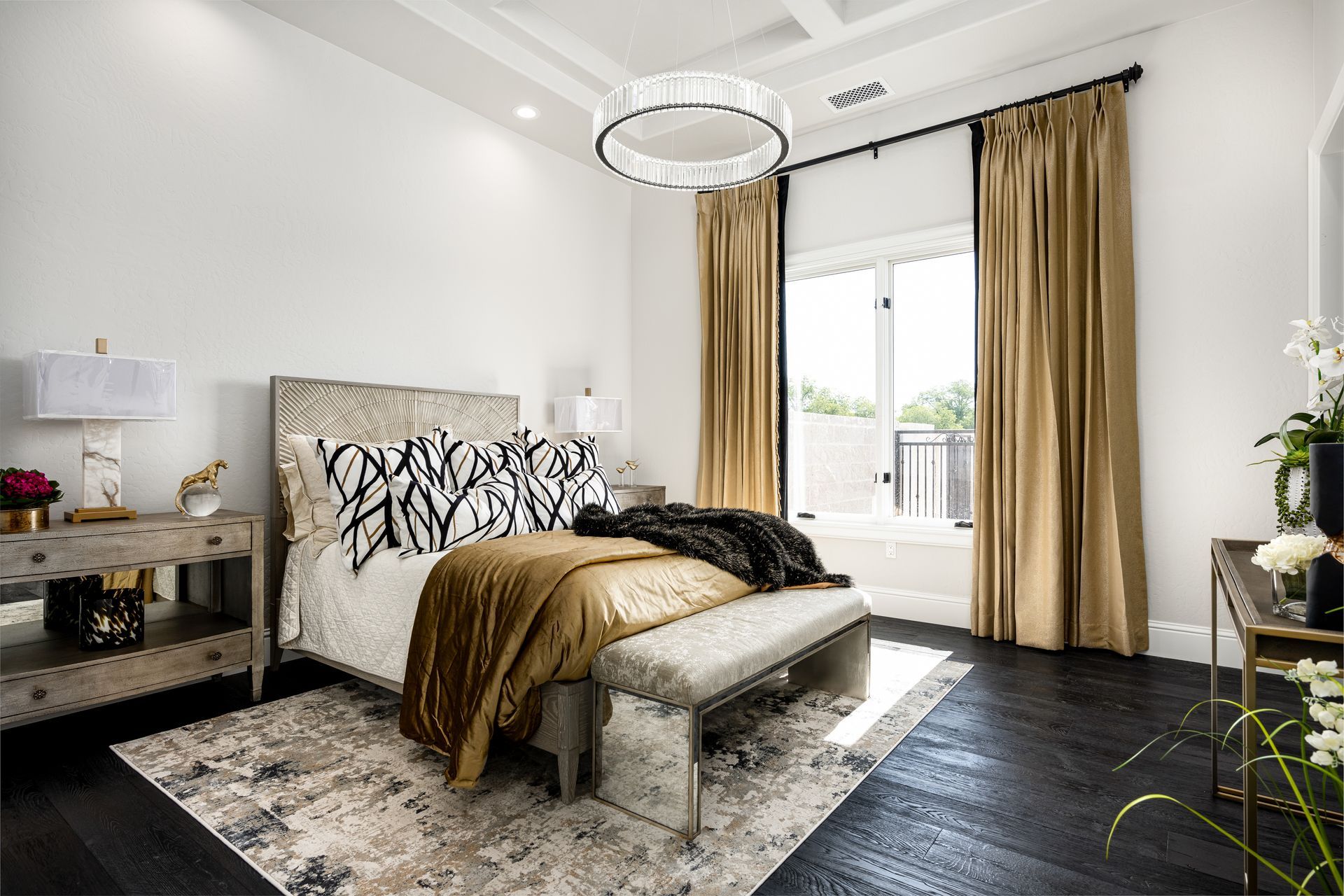 Bedroom with a bed, bench, rug, and dark wood floor; gold curtains and a chandelier.
