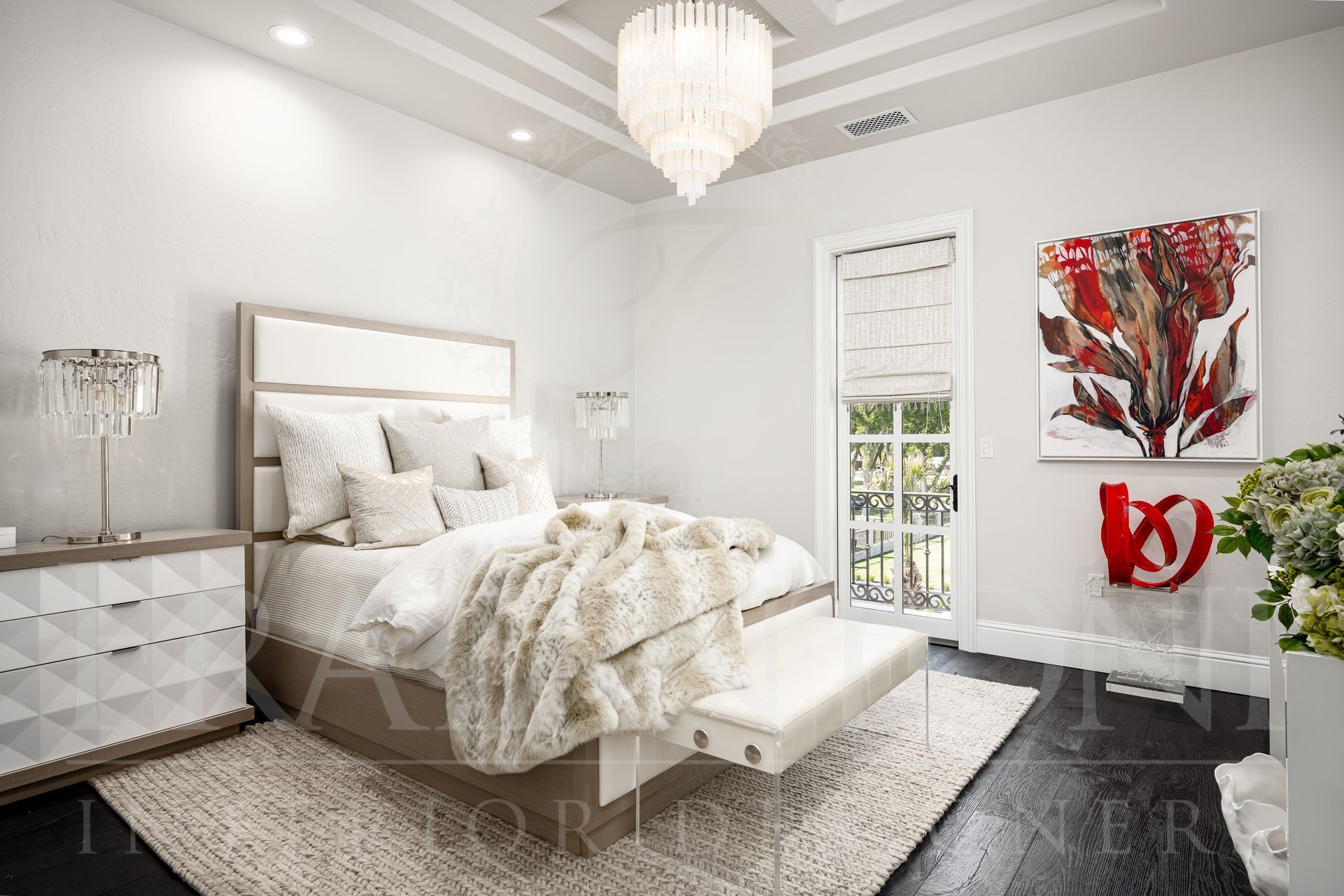 Elegant white bedroom with a bed, nightstand, art, ceiling details, bedside table lamps, and chandelier.