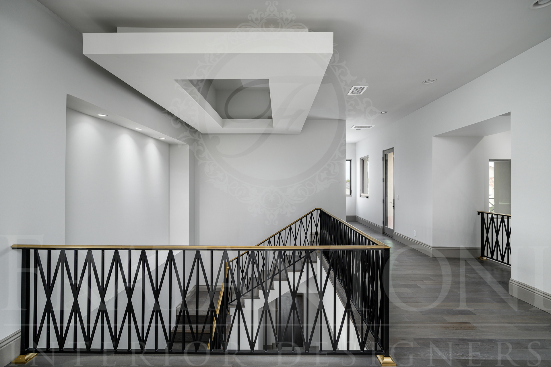 luxury walkway with custom black railing overlooking staircase and a modern ceiling opening. Dark floors, statement ceiling