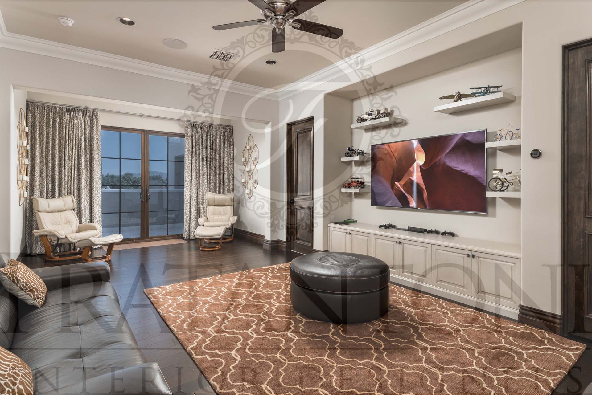 Transitional movie room with dark sofa, patterned rug, TV, built-in shelving and storage, and large glass doors to a balcony.