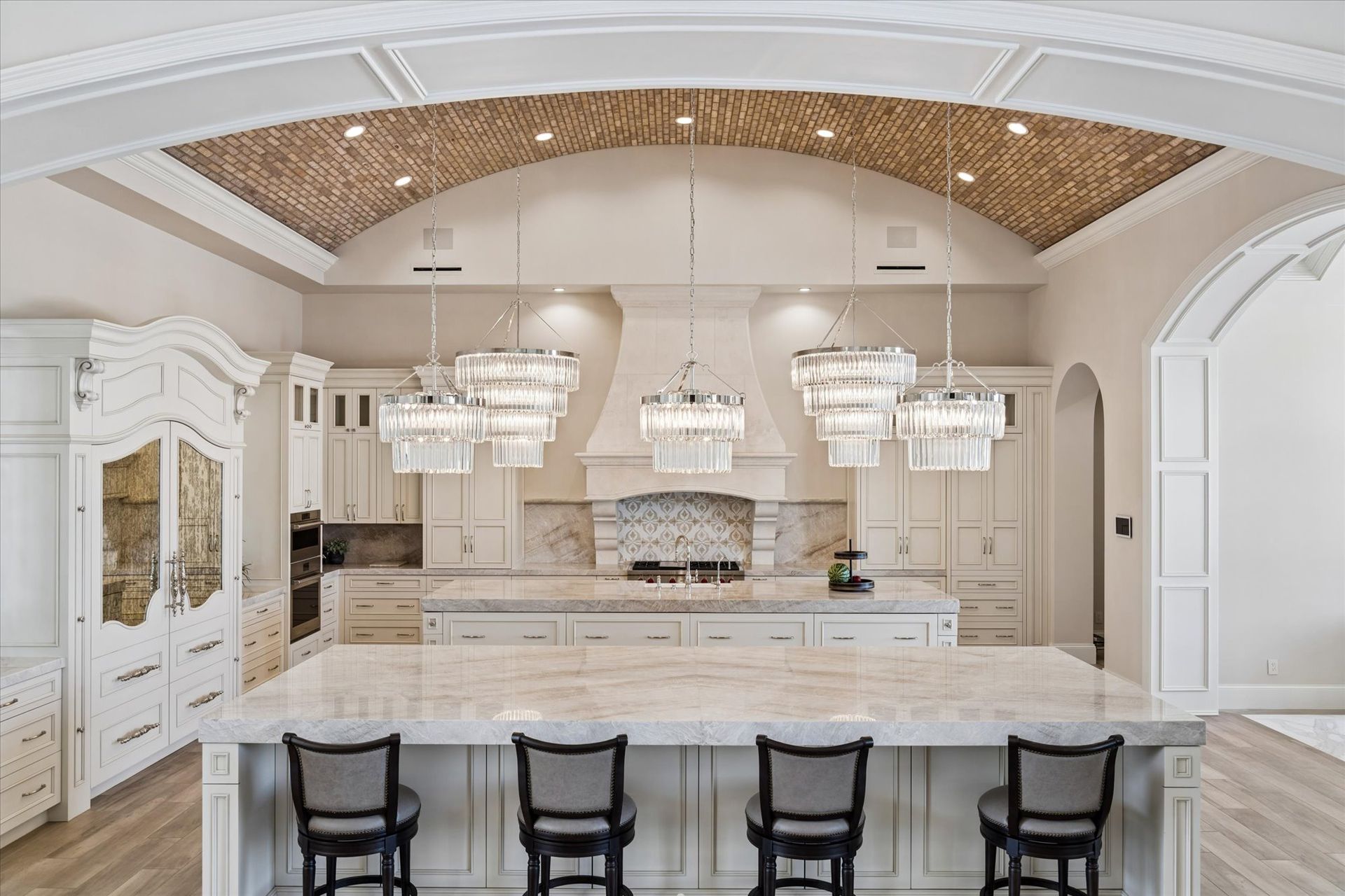 Luxury kitchen with dual marble islands, armoire hidden fridge, barrel brick ceilings and large chandeliers