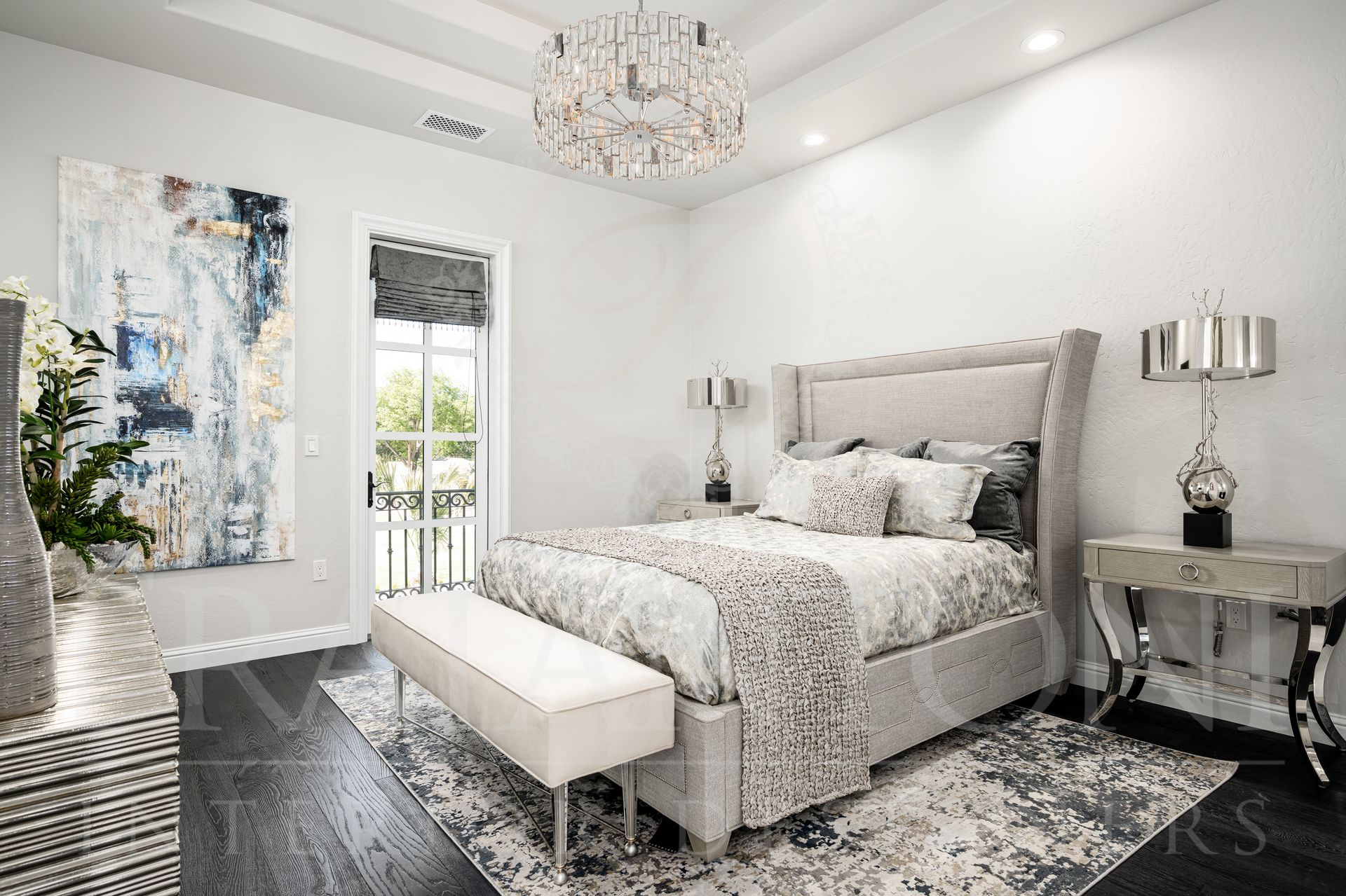 Elegant bedroom with a chandelier, large artwork, dark wood floors, and a neutral color palette.