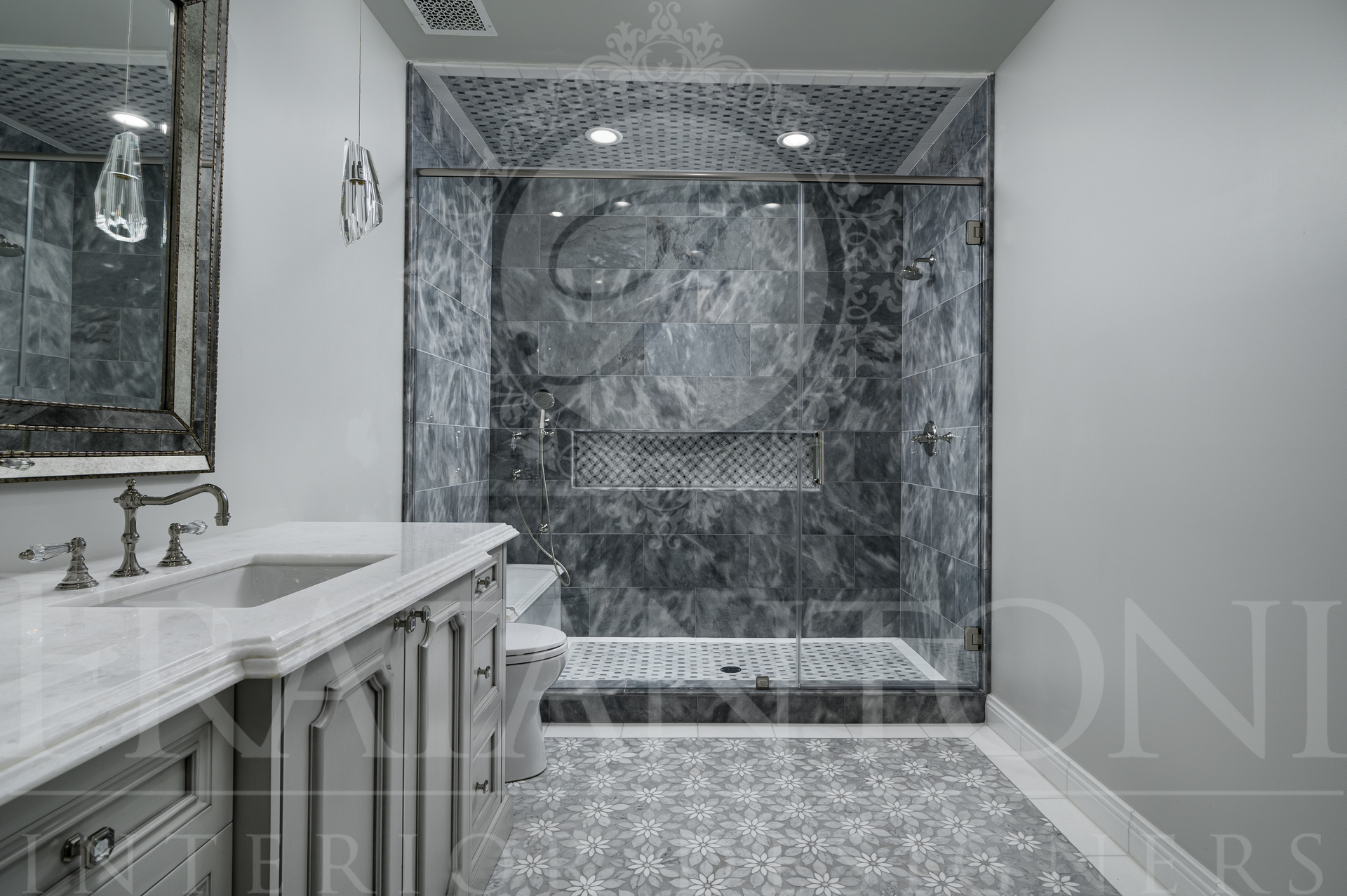 Luxury marble bathroom with double vanity, large mirror, mosaic tile floors, brass hardware, and tiled walk-in shower with a shower bench and shower niche designed by Fratantoni Interior Designers.