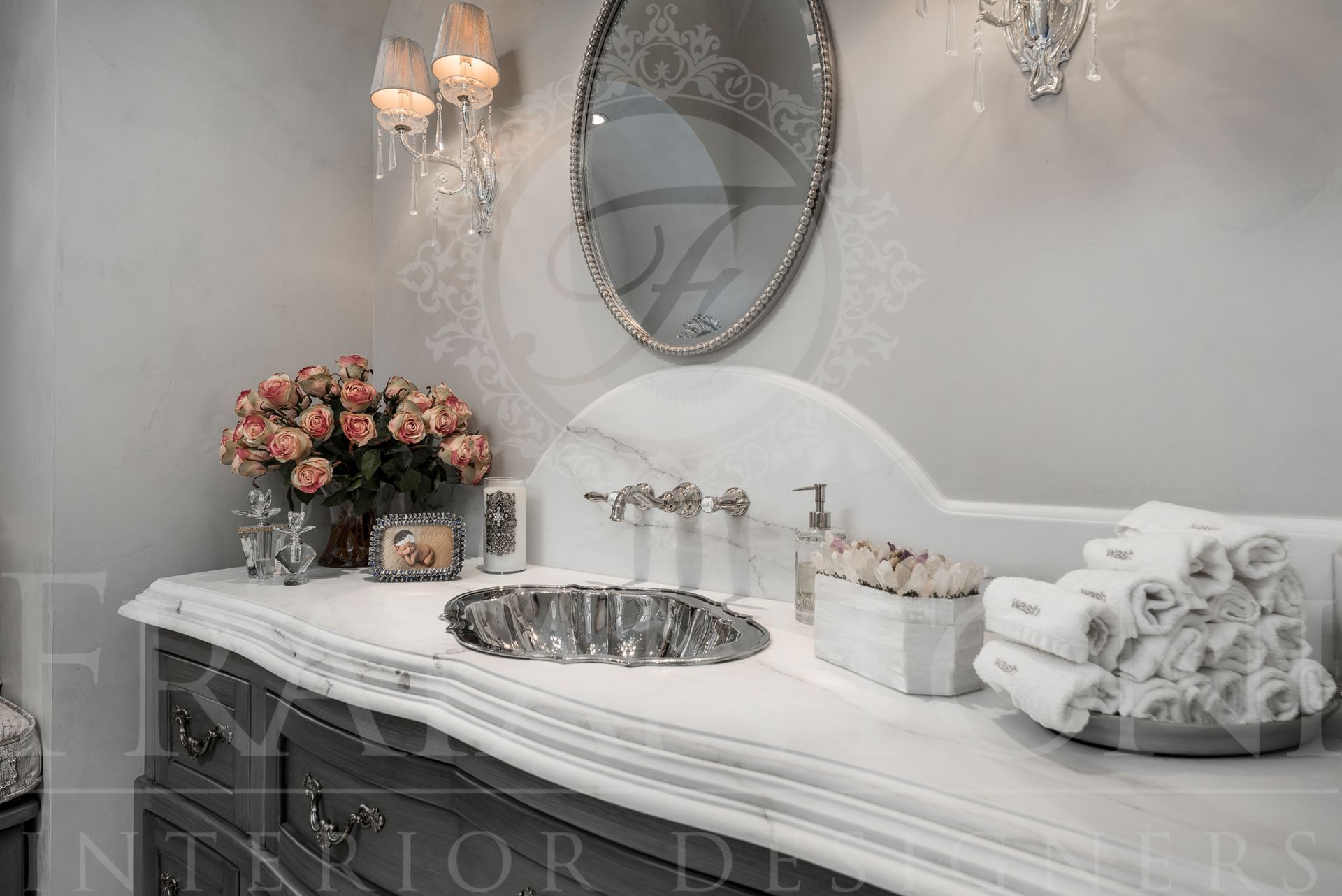 Elegant bathroom with marble vanity, oval mirror, and floral arrangement. White towels, silver fixtures.