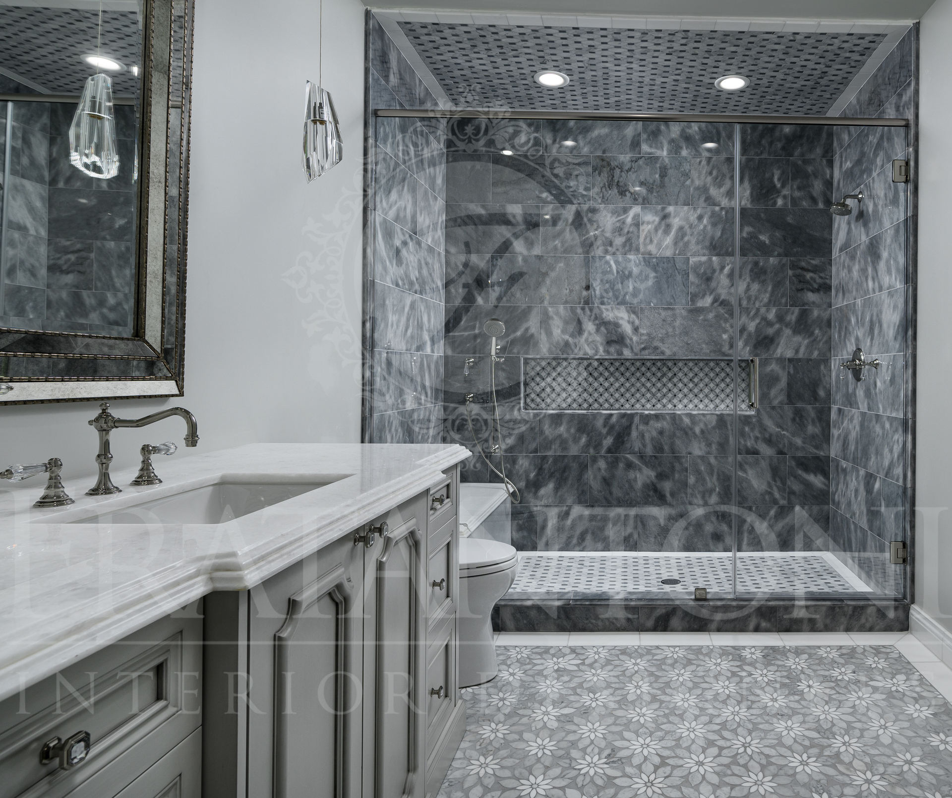 Luxury marble bathroom with custom vanity, large mirror, and glass-enclosed shower in gray tones. Features mosaic floor tiles and brass accents.