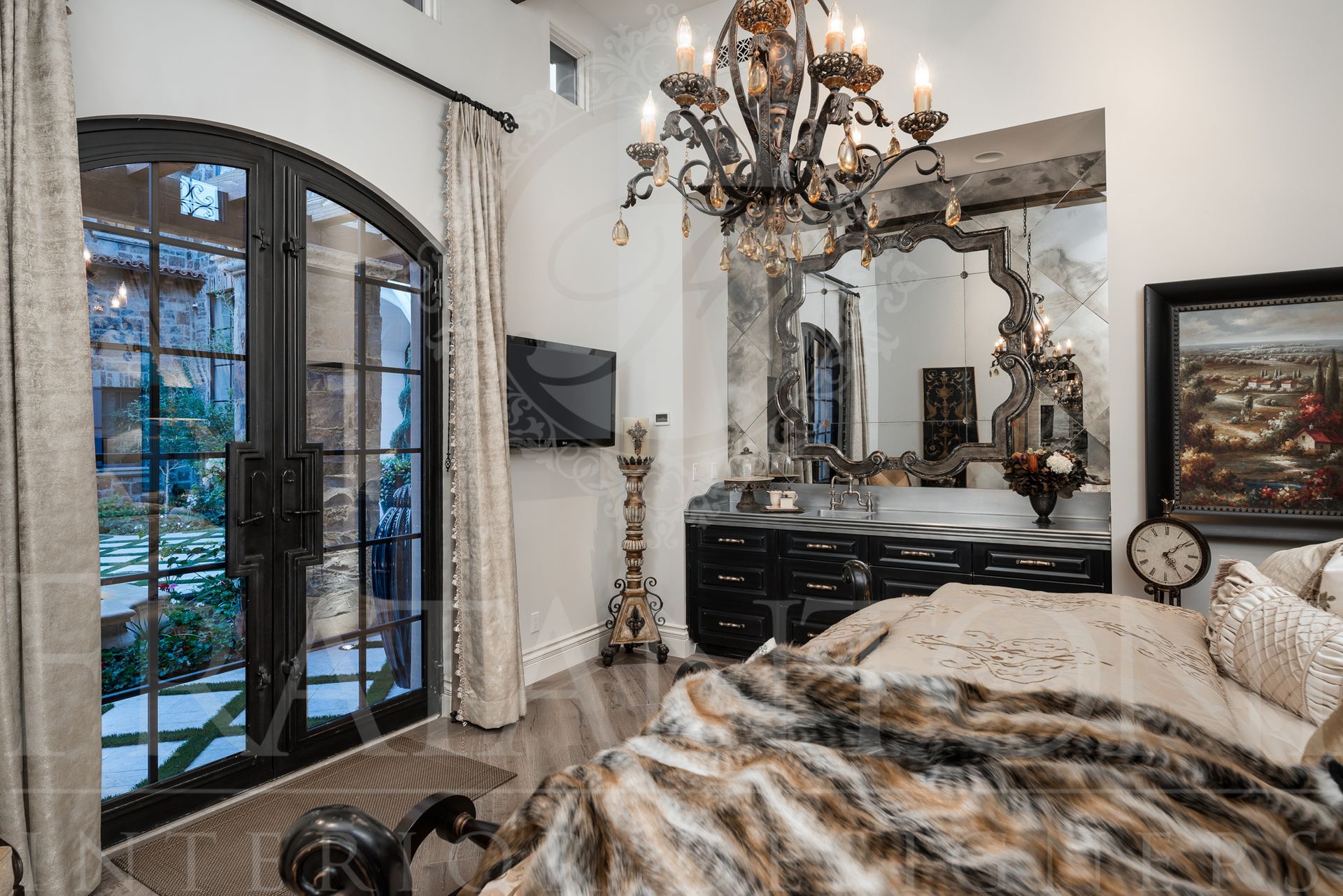 Elegant bedroom with arched door with courtyard views,, chandelier, dresser, and faux fur blanket.