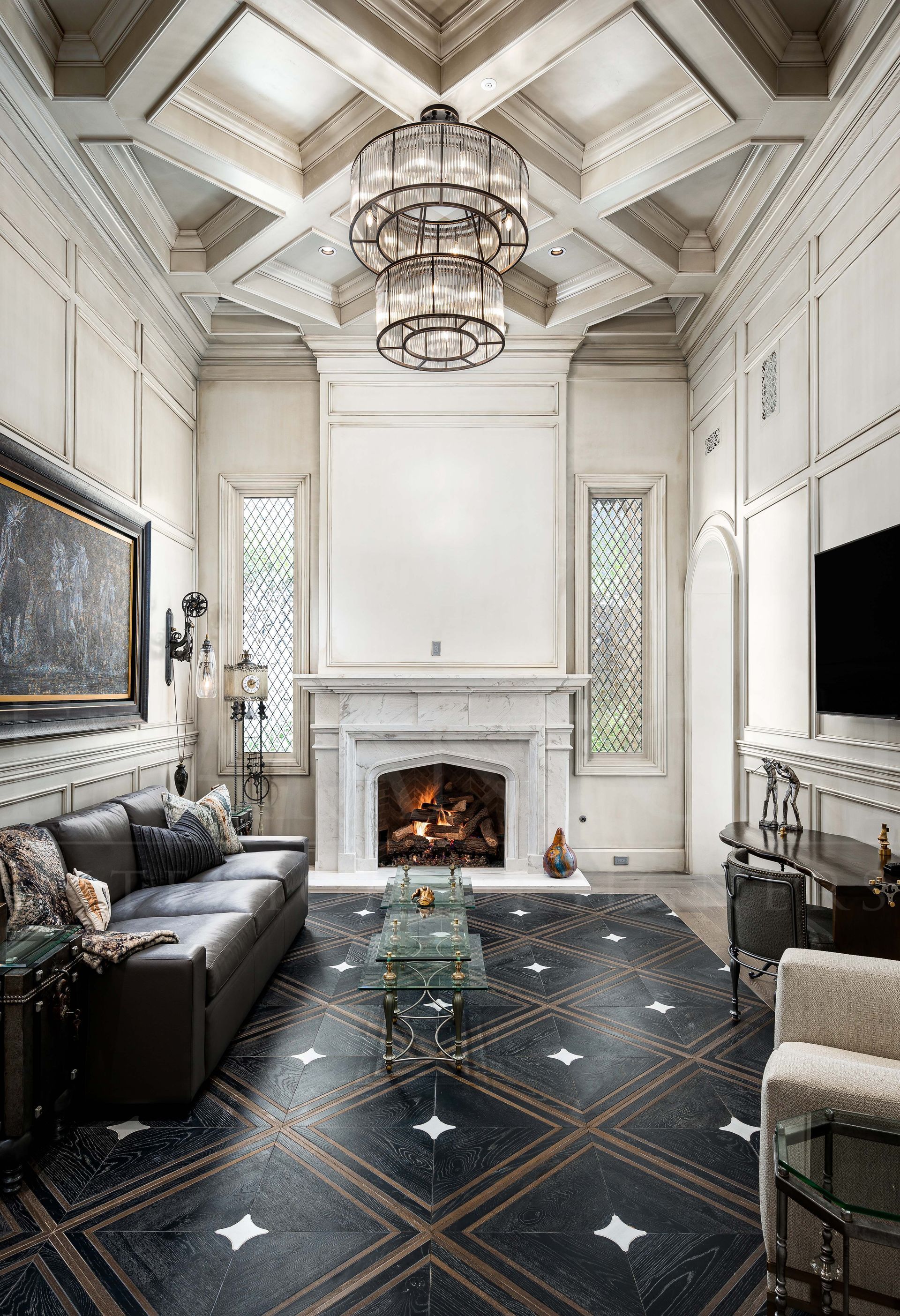 Luxury home office with a black sofa, marble fireplace, chandelier, ornate ceiling, and dark patterned wood floors