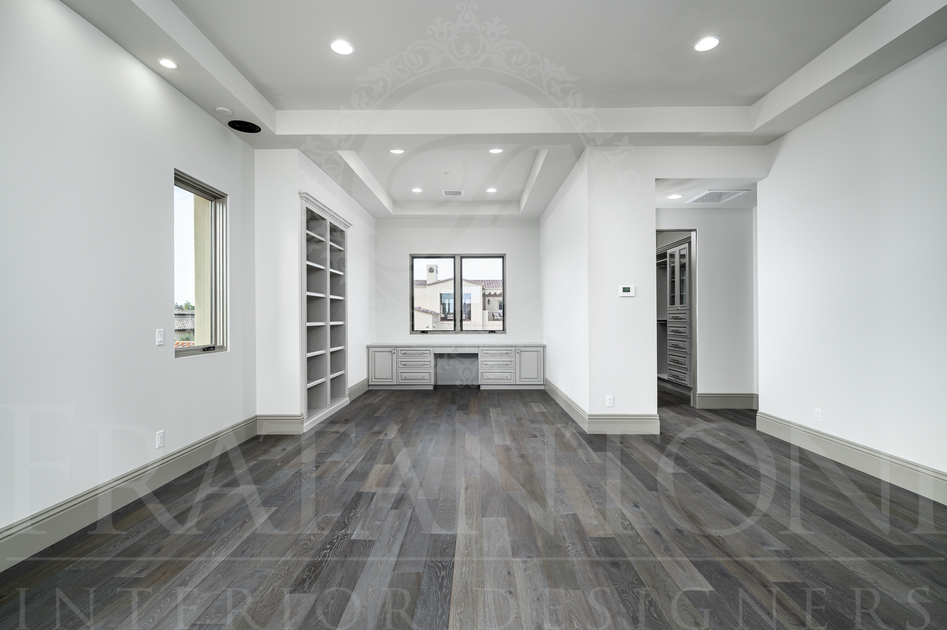 Custom luxury office with dark wood floors, white walls, recessed ceiling lights, a custom built-in desk, and built-in shelving.