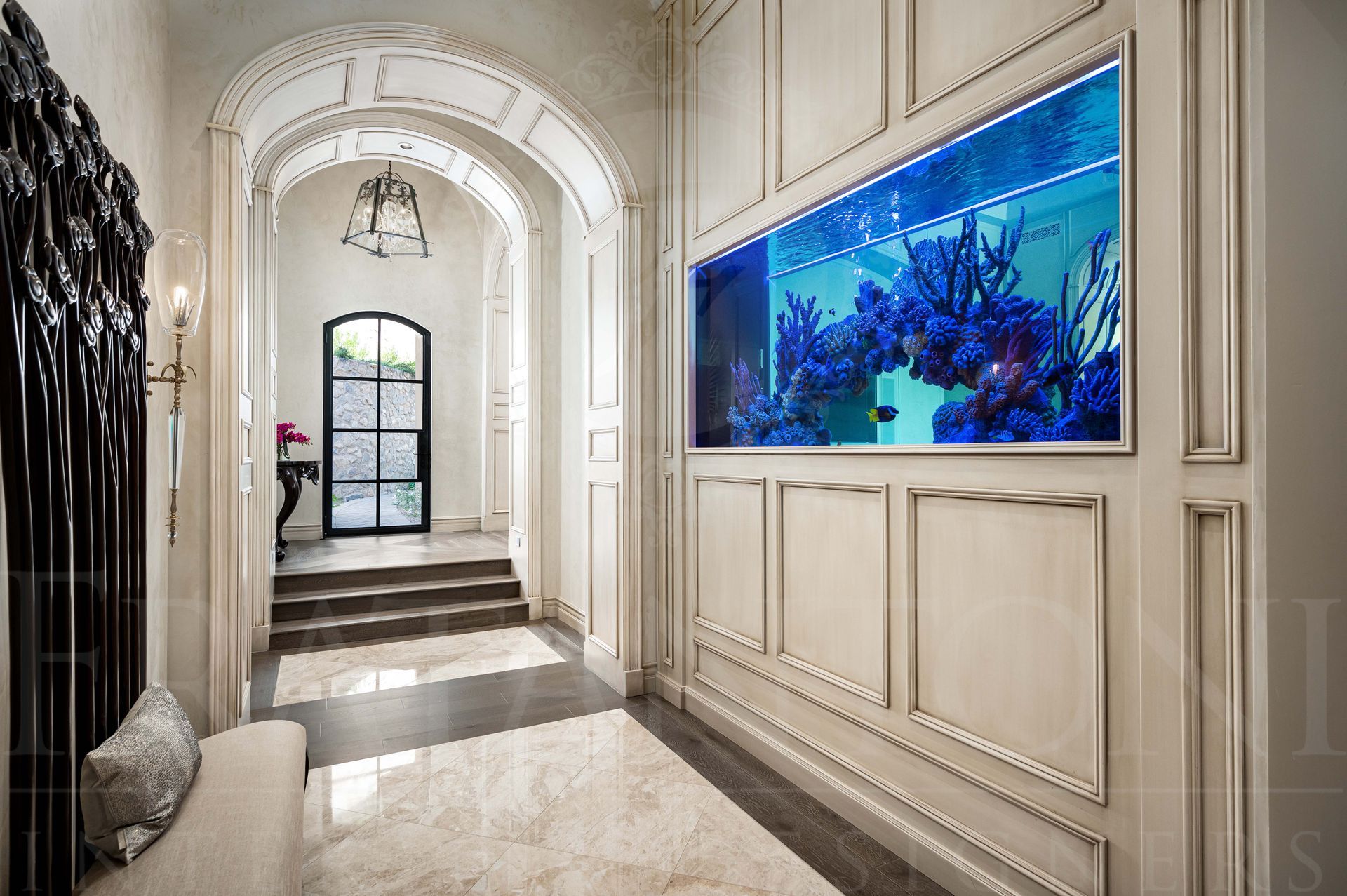 Elegant hallway with arched doorways, marble floors, paneled walls, and a large in-wall aquarium on the right