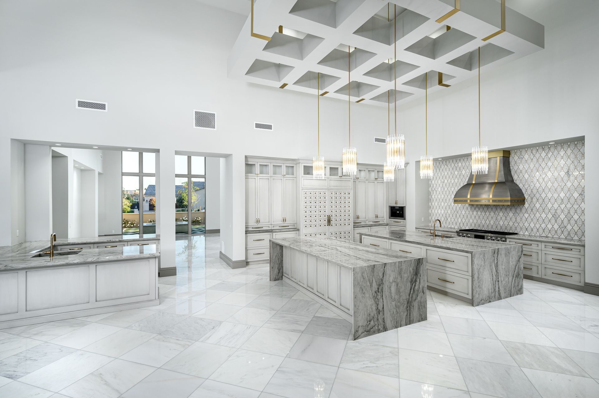 Spacious, all-white kitchen with marble counters, pendant lights, and a decorative ceiling.