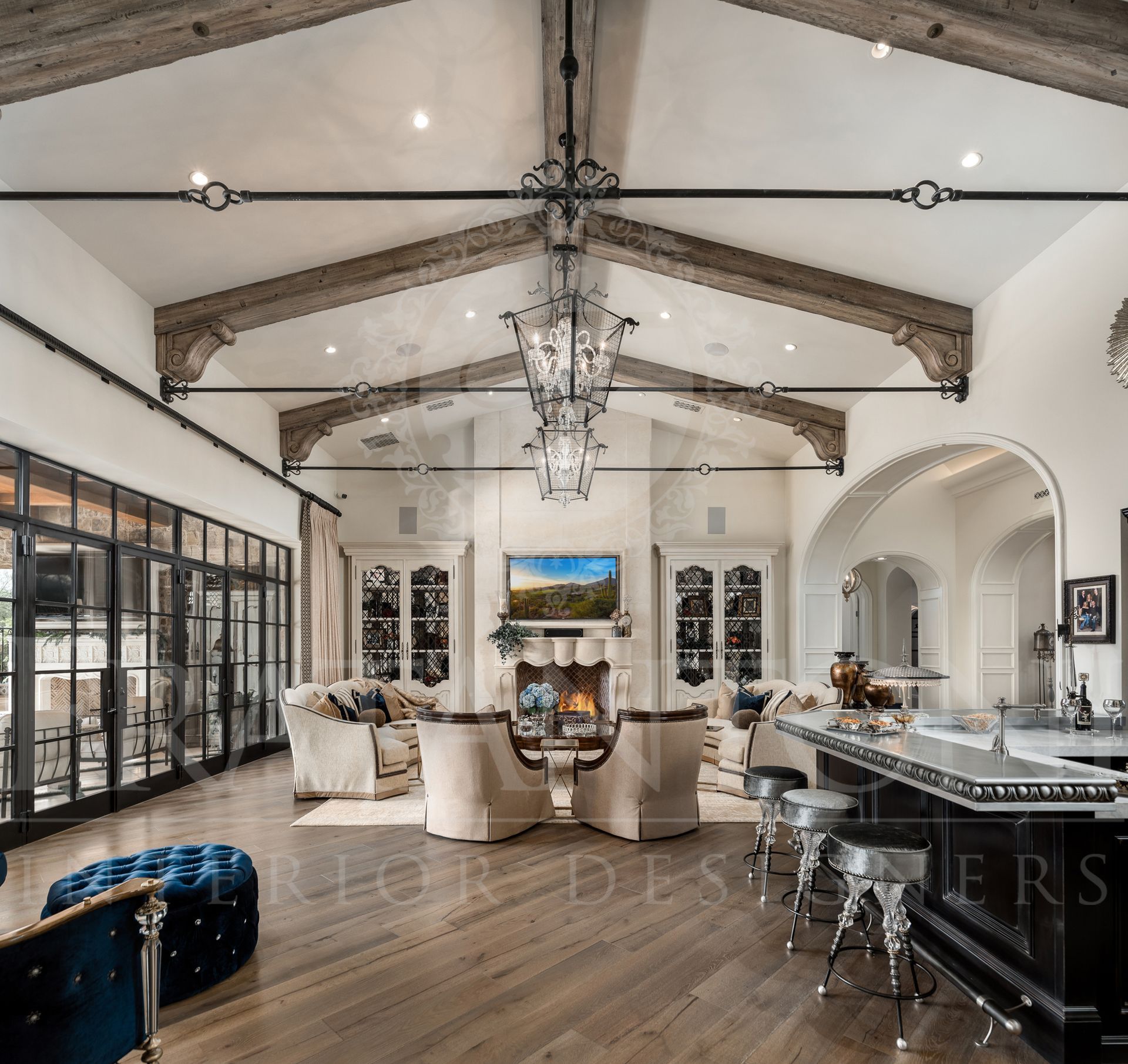 Spacious living room with vaulted ceiling, wood beams, carved stone fireplace, wood floors, and bar.