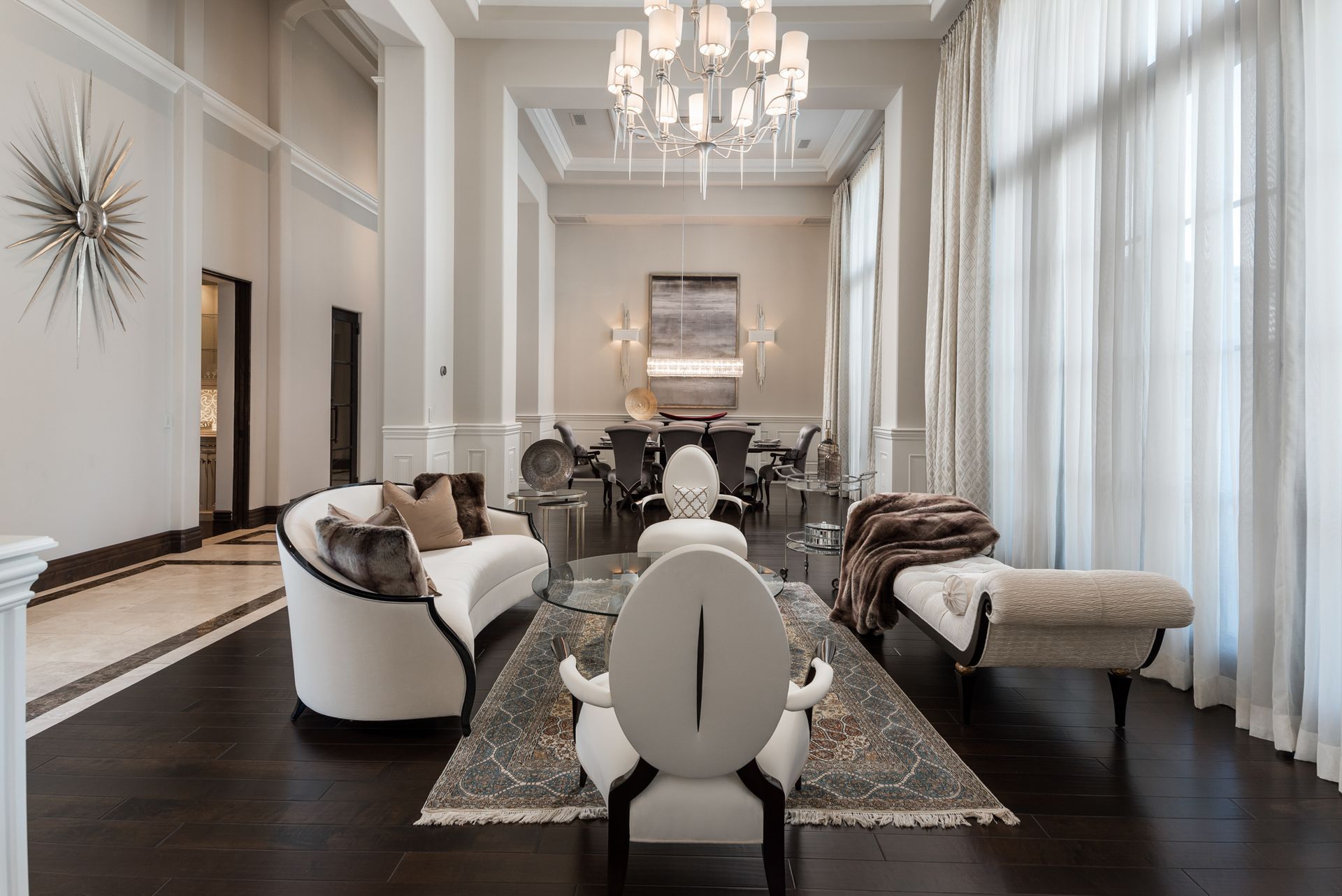 Elegant living room with white and gray decor; curved sofa, chaise lounge, chandelier, dark wood floors.