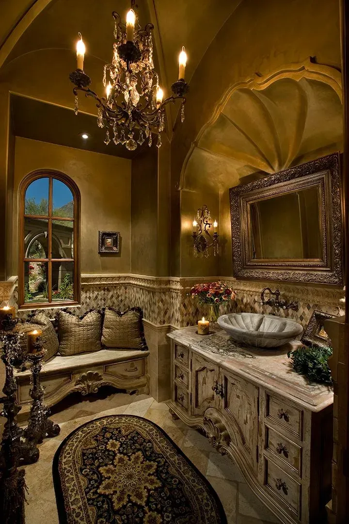 Ornate, gold-toned bathroom with chandelier, bench, stone sink, and detailed carved cabinetry.