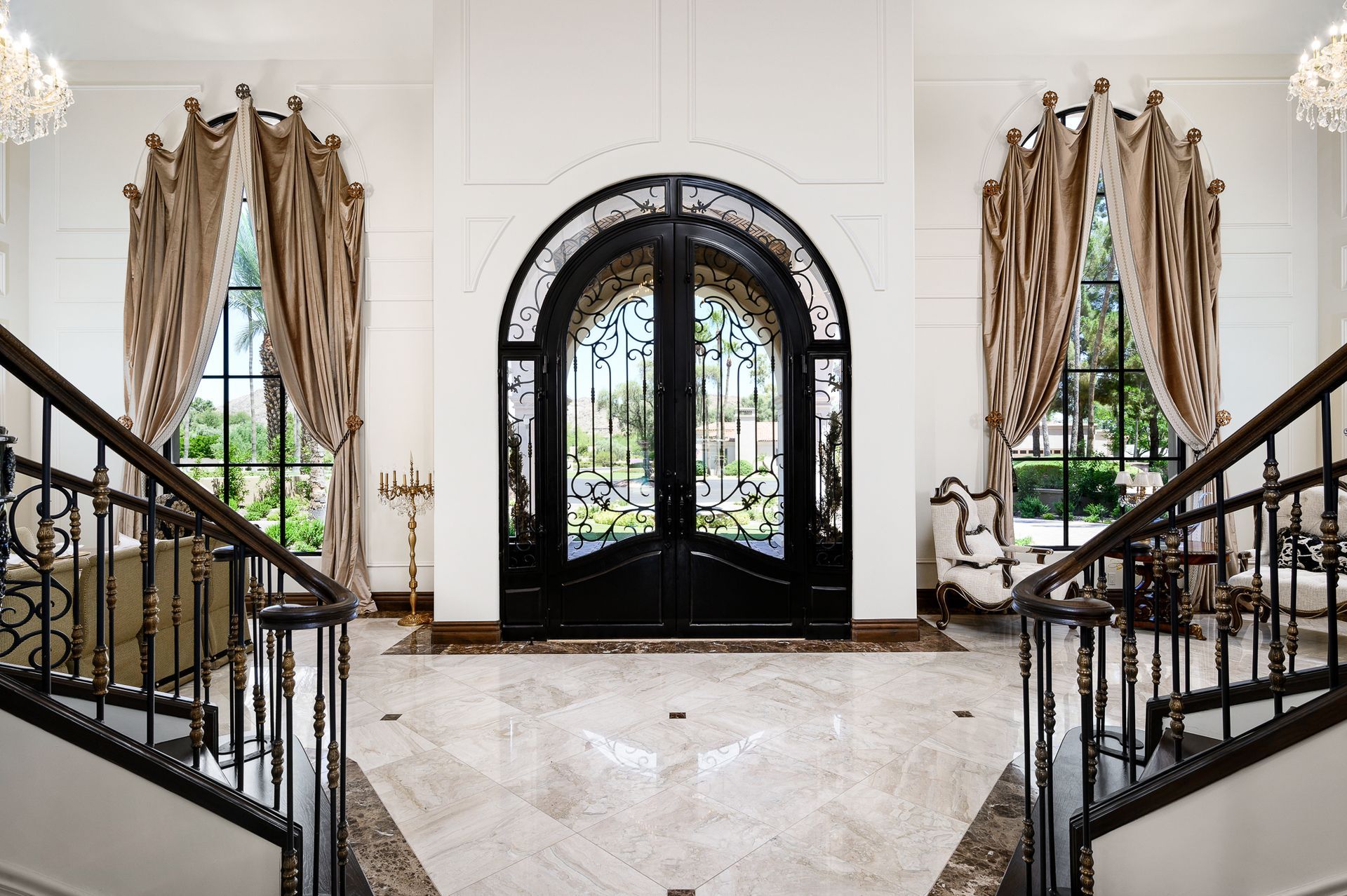 Grand entry hall with black arched double doors, wrought-iron stair railings, and tall draped windows