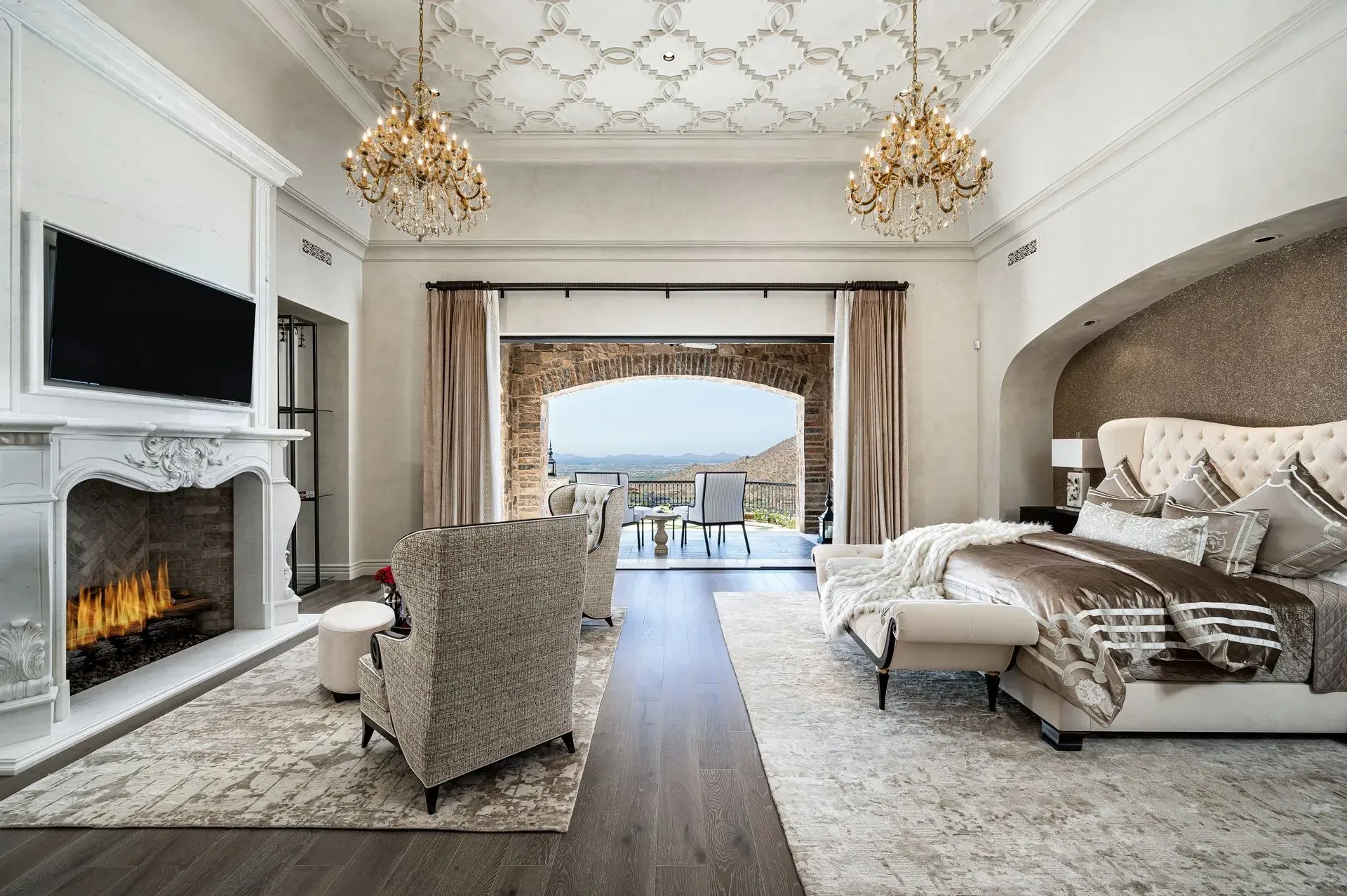 Luxurious bedroom with fireplace, chandelier, balcony view, and large bed.