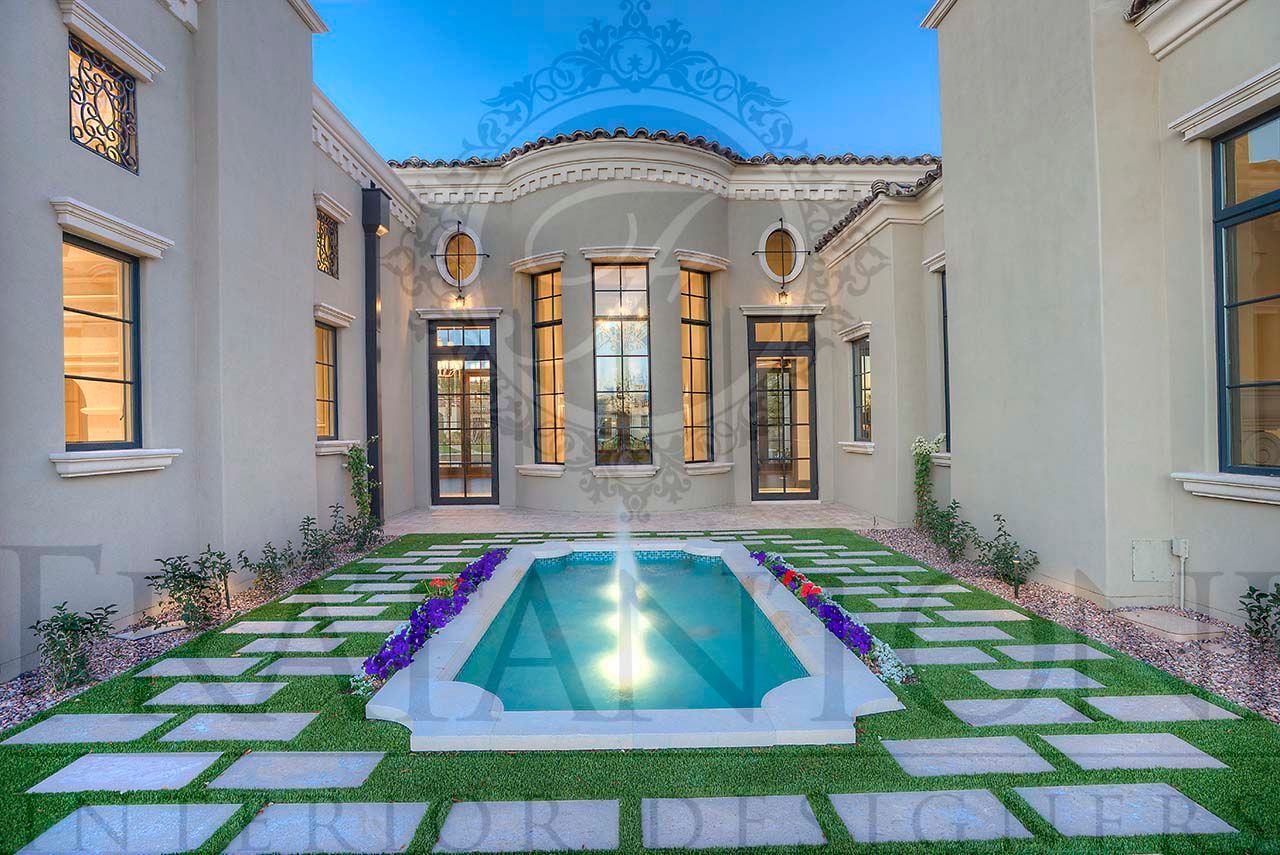 Mediterranean villa courtyard with a small turquoise fountain, stone pavers, and large windows under a blue-lit evening sky in paradise valley arizona