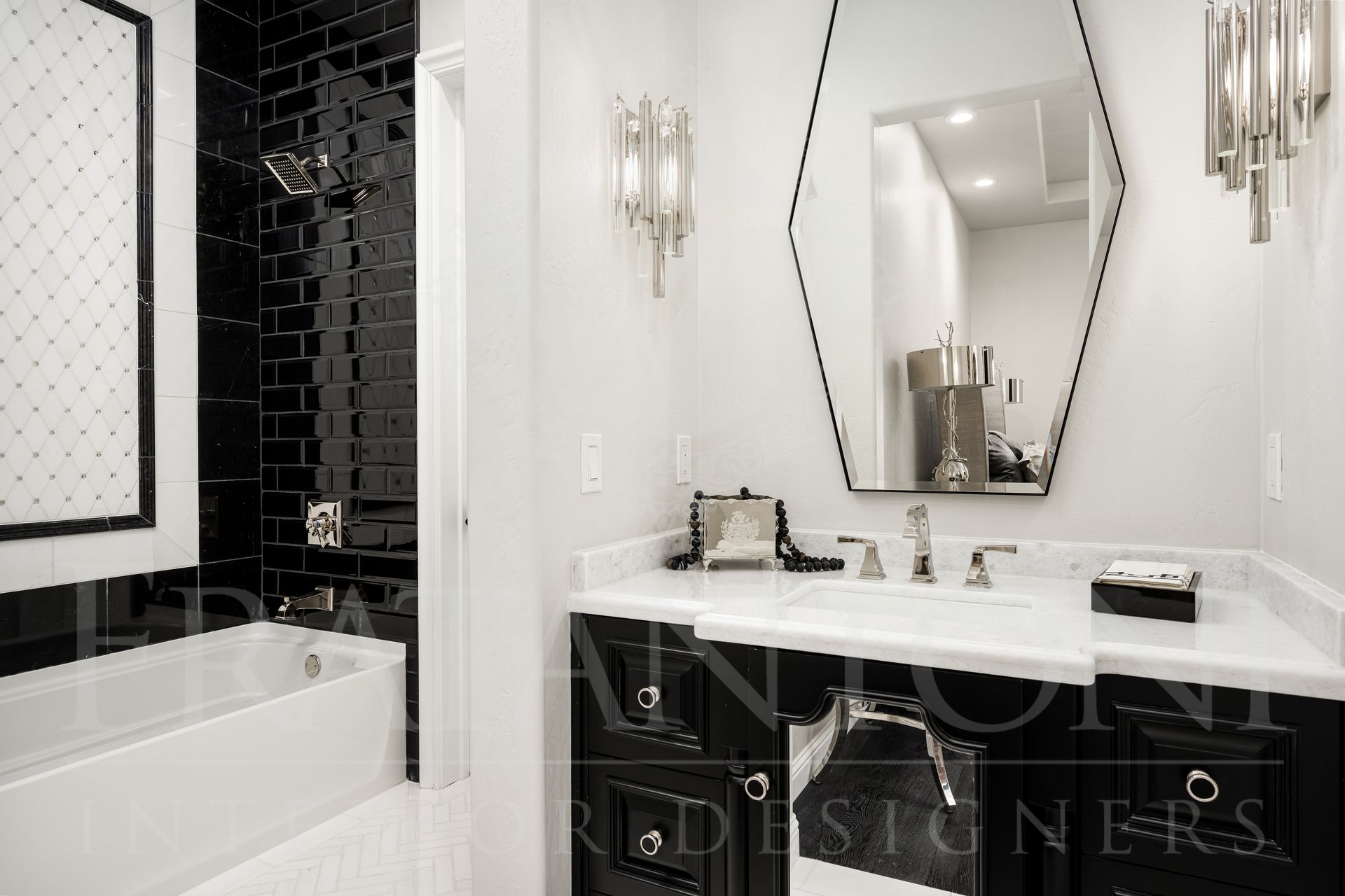 Modern black and white bathroom with marble countertop, black vanity, hexagon mirror, and sconces.