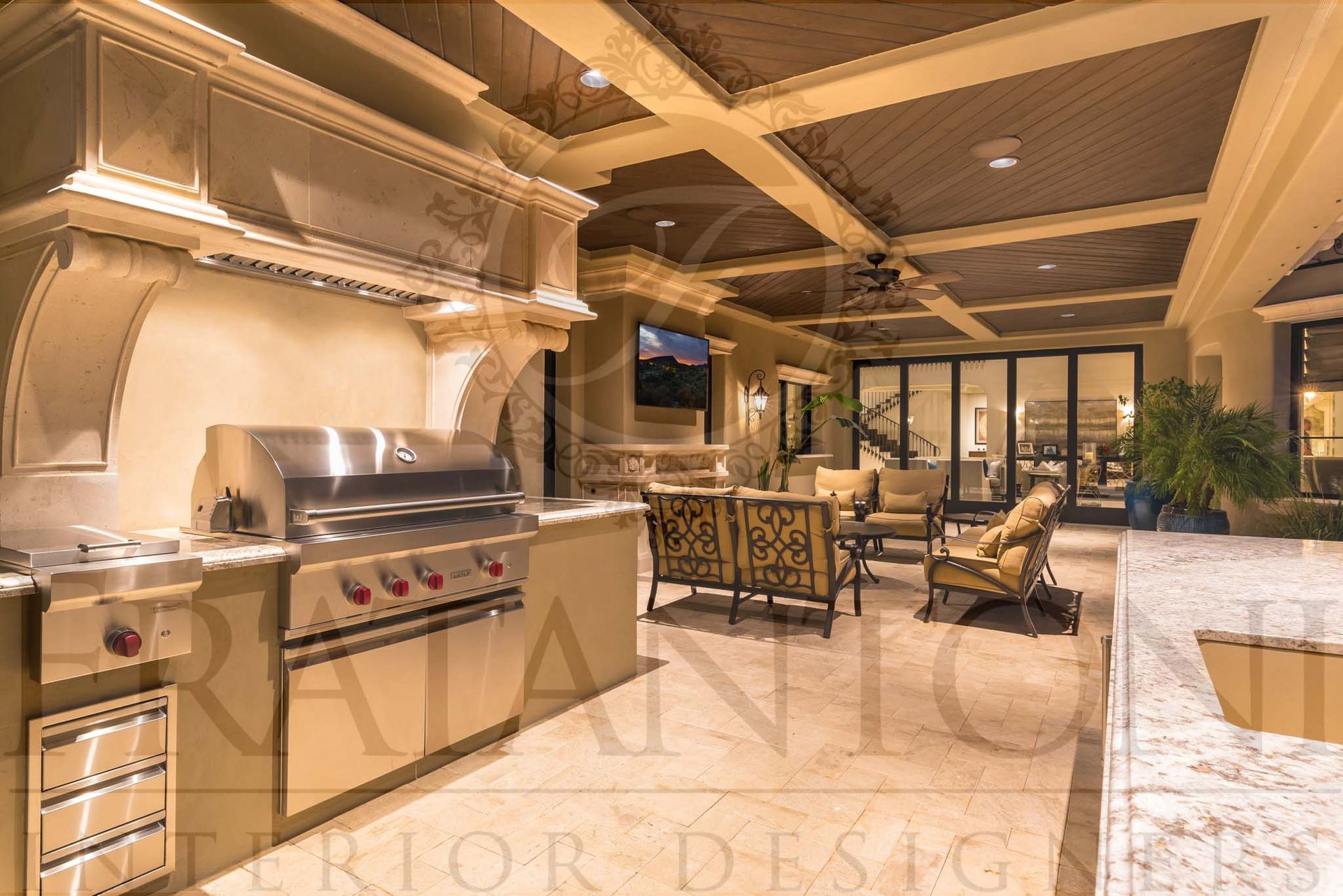 Luxury outdoor kitchen and dining patio with a stainless grill, stone counters, coffered ceilings, and warm lighting at dusk designed by luxury interior designers in arizona