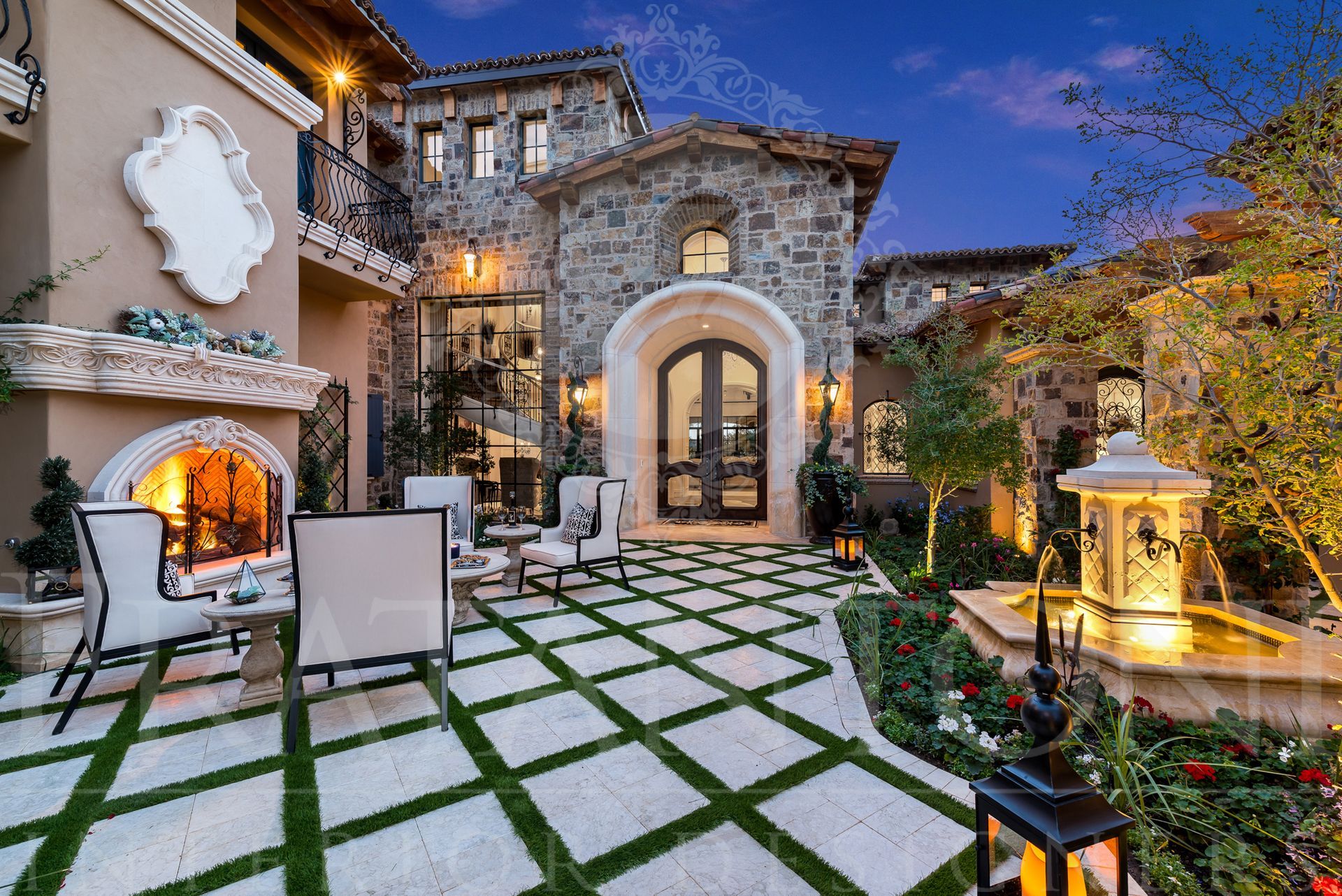 Luxurious stone villa exterior with outdoor seating, fireplace, fountain, and manicured landscaping at dusk designed by Fratantoni Interior Designers
